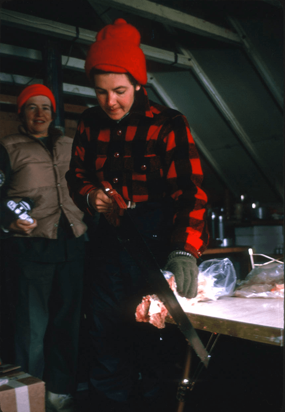 A woman in a red and black shirt cuts a steak with a saw.