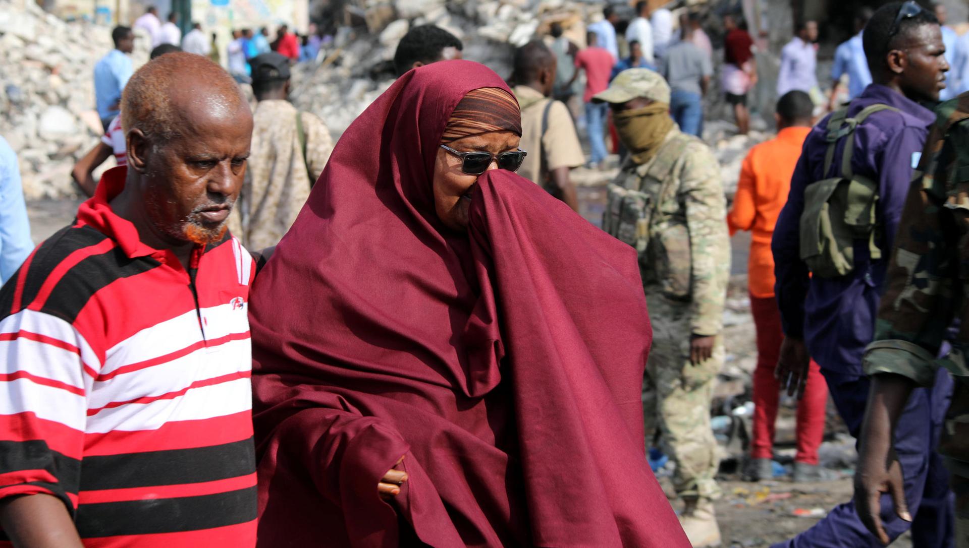 A woman holds her hand over her face and clutches the arm of a man next to her as they walk through the destroyed shopping district in Mogadishu. 