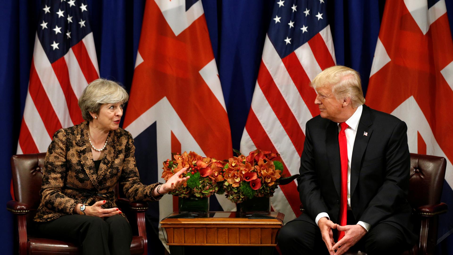 President Donald Trump sits across from Prime Minister Theresa in front of US and British flags.