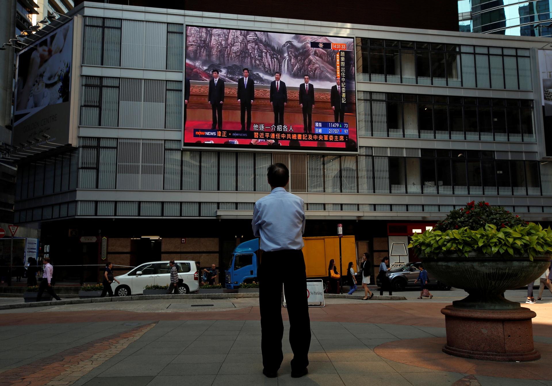 A man watches a news broadcast of China's President Xi Jinping and other new Politburo Standing Committee members attending a meeting in Beijing, outside a commercial building in Hong Kong.