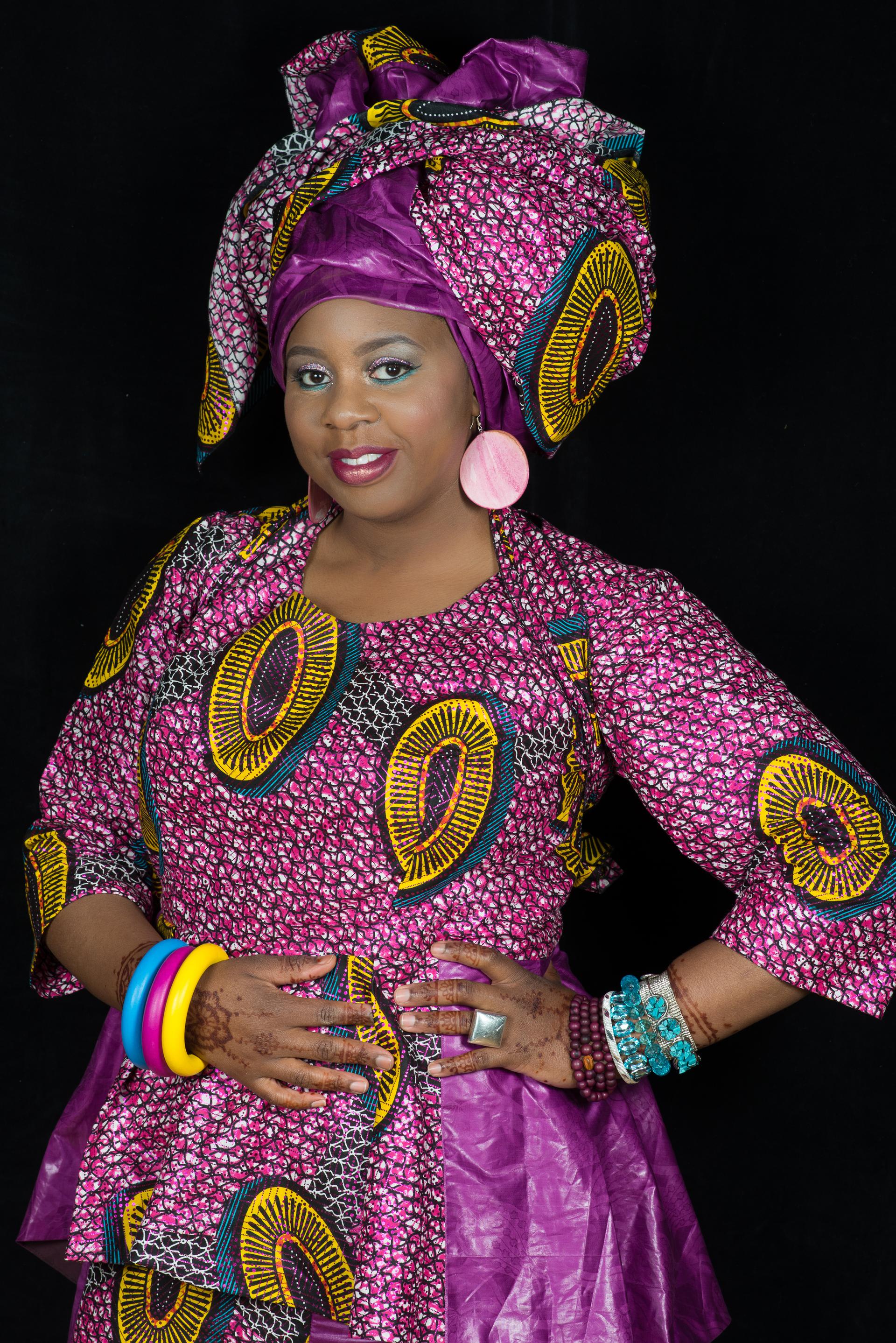 A woman is wearing a colorful pink dress and matching bright headwrap.