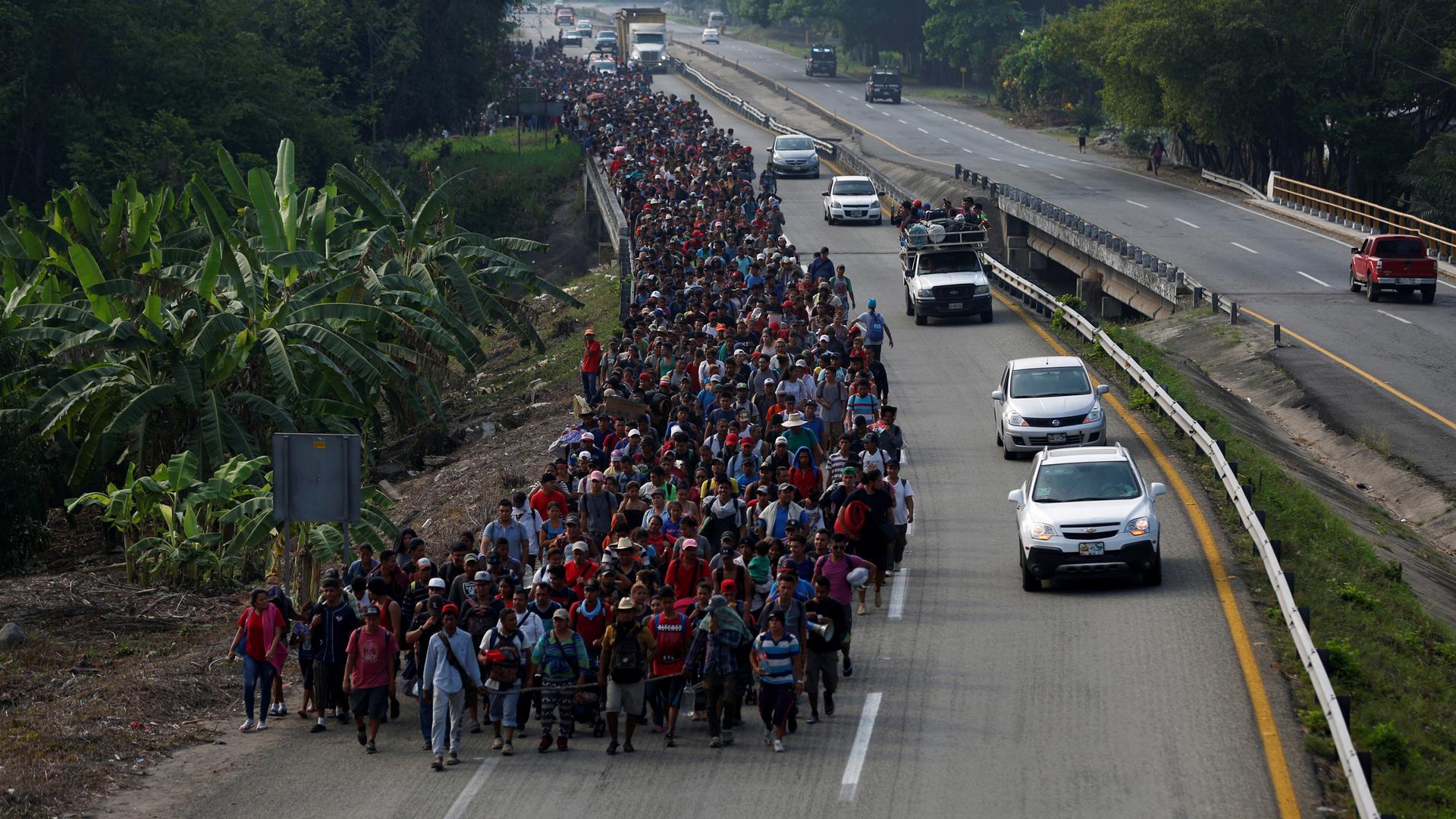 A long line of people, hundreds and hundreds, walk in one lane of a highway in a large mass.