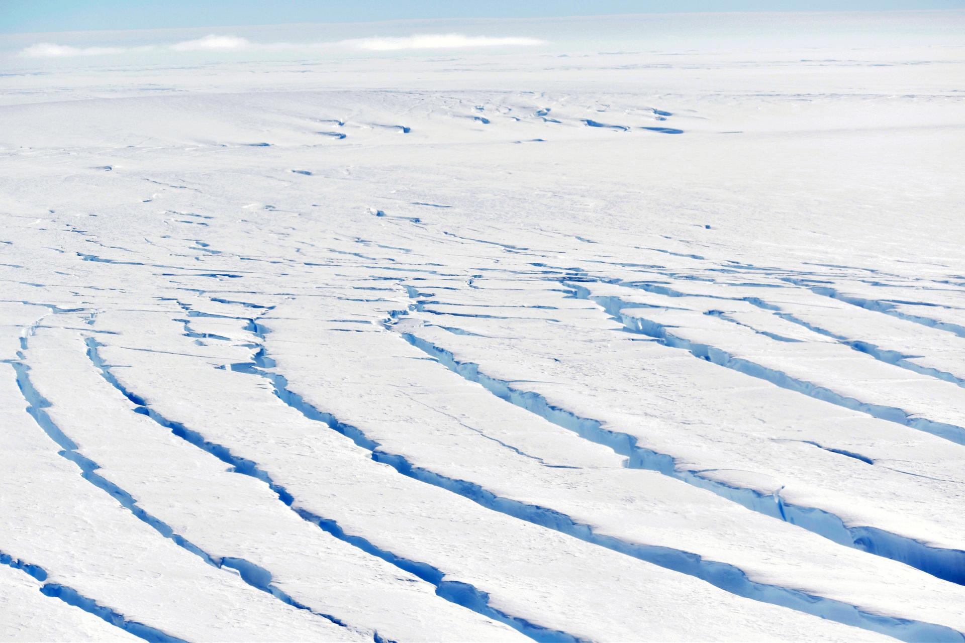Dark blue crevasses ripple across the frozen surface of an icy white horizon