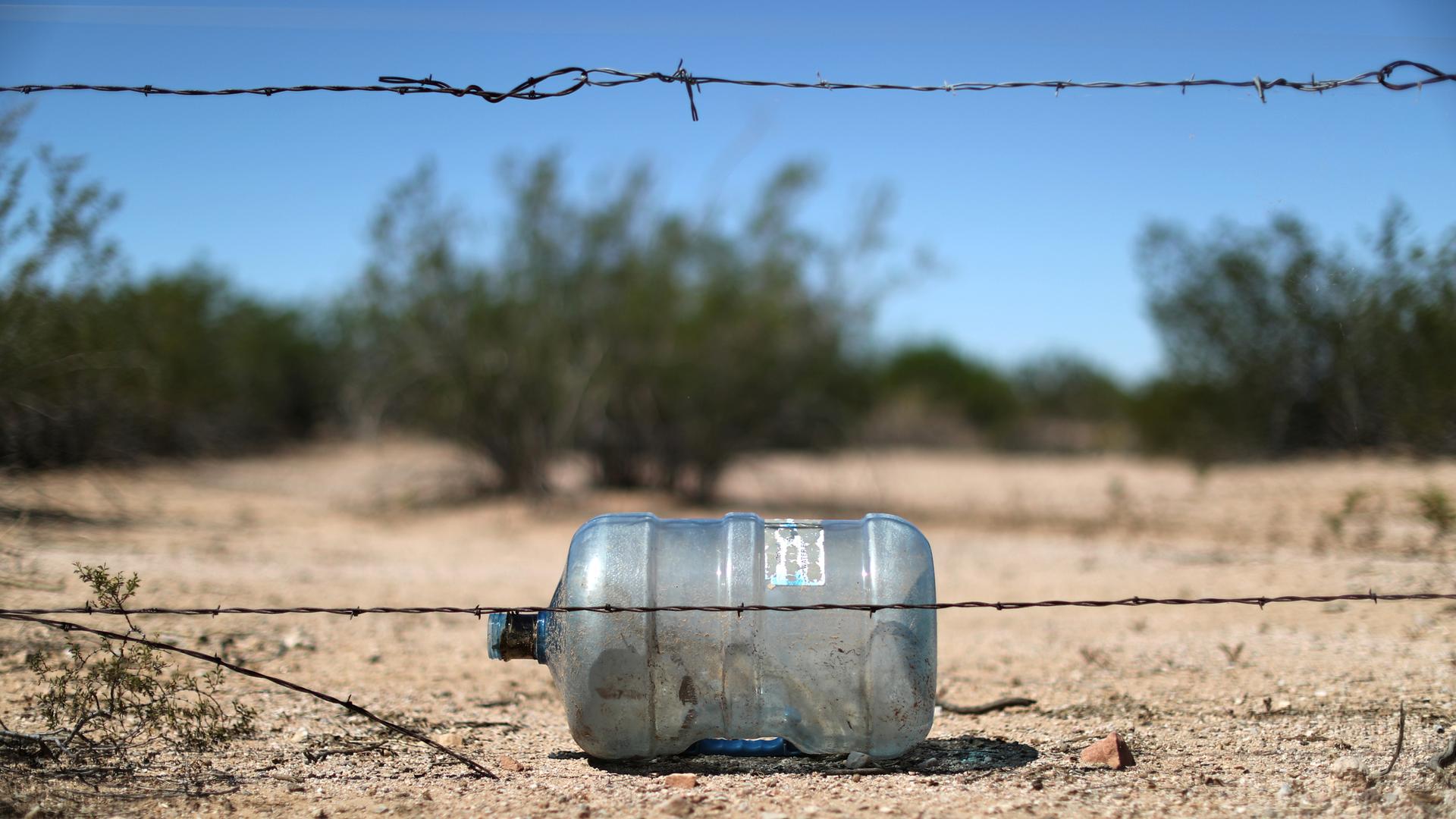 An empty water bottle lays on the dirt behind a string of barbed wire