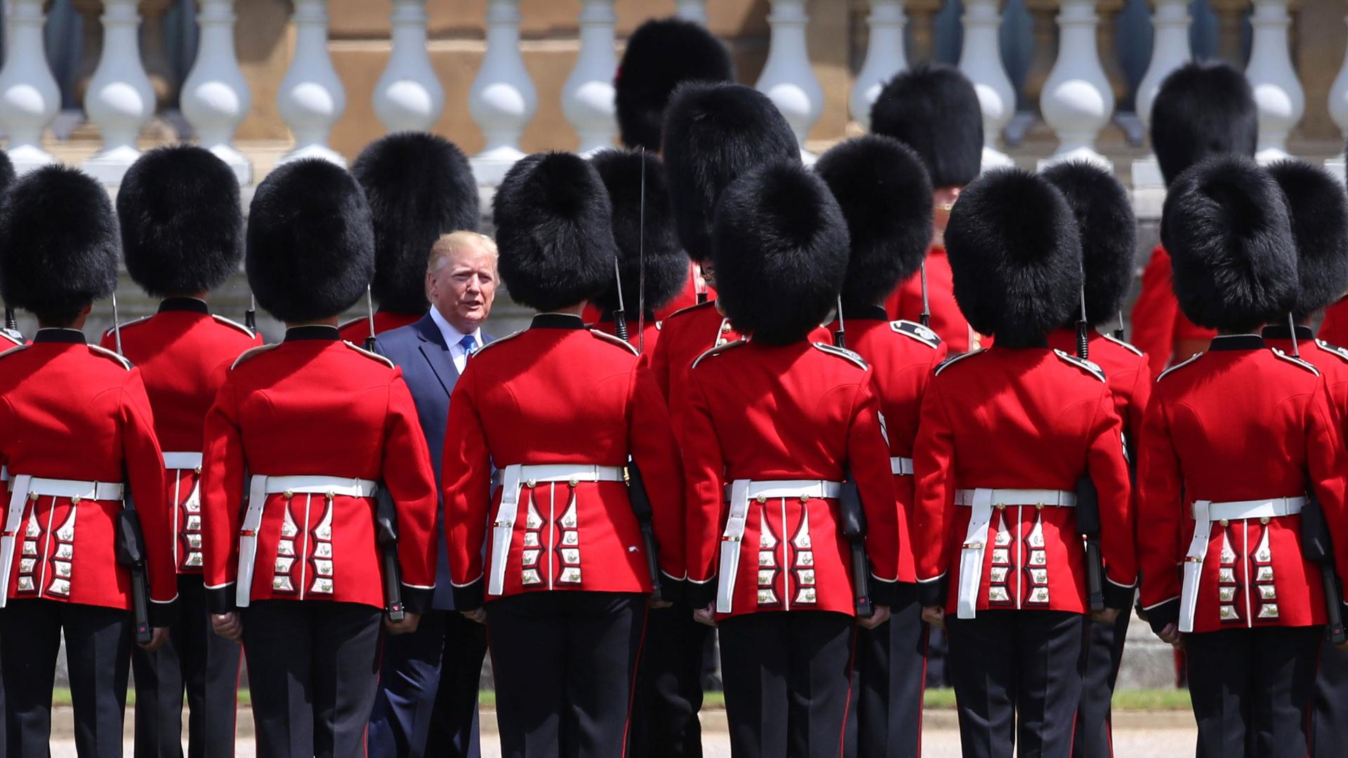 Donald Trump is shown standing among more than a dozen of the Royal honor guard dressed in traditional red uniforms and tall black hats.