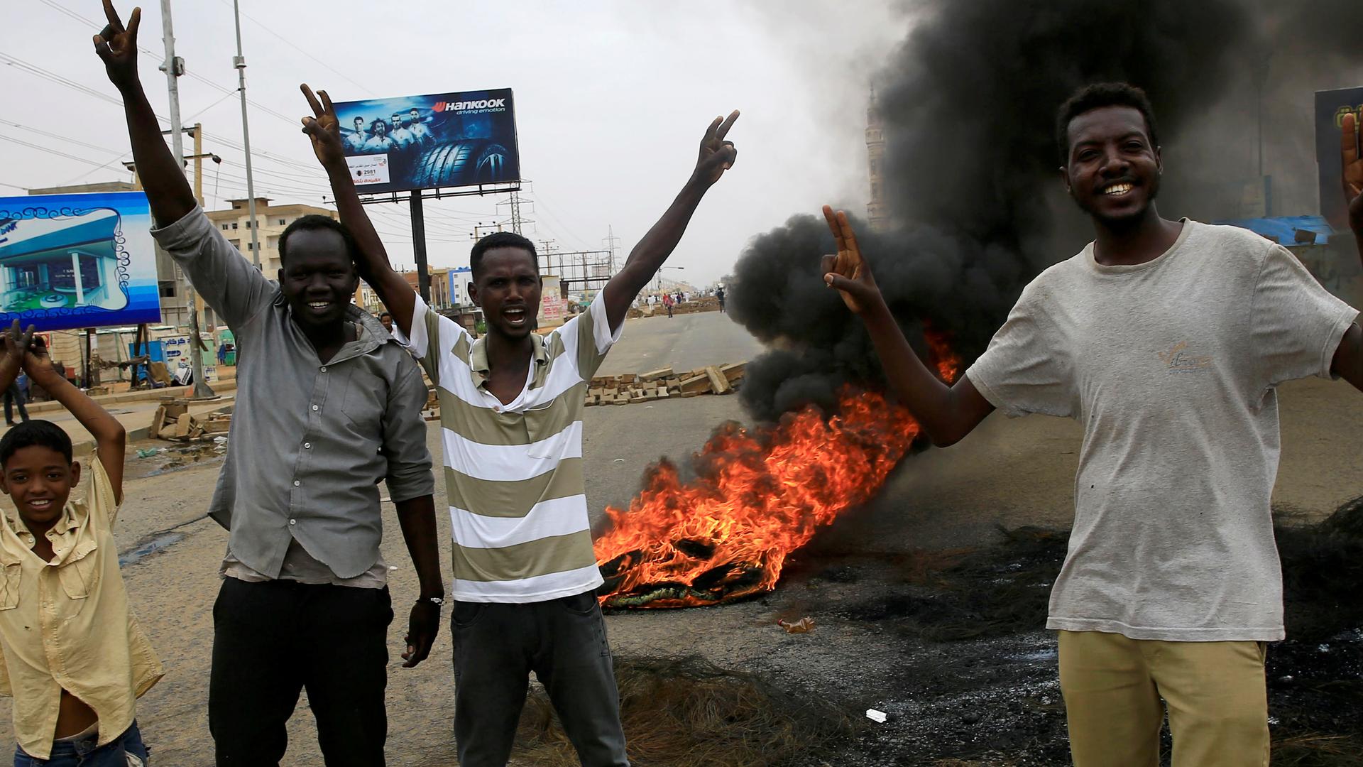 Sudanese protesters gesture near burning tires used to erect a barricade on a street, demanding that the country's Transitional Military Council handover power to civilians. 