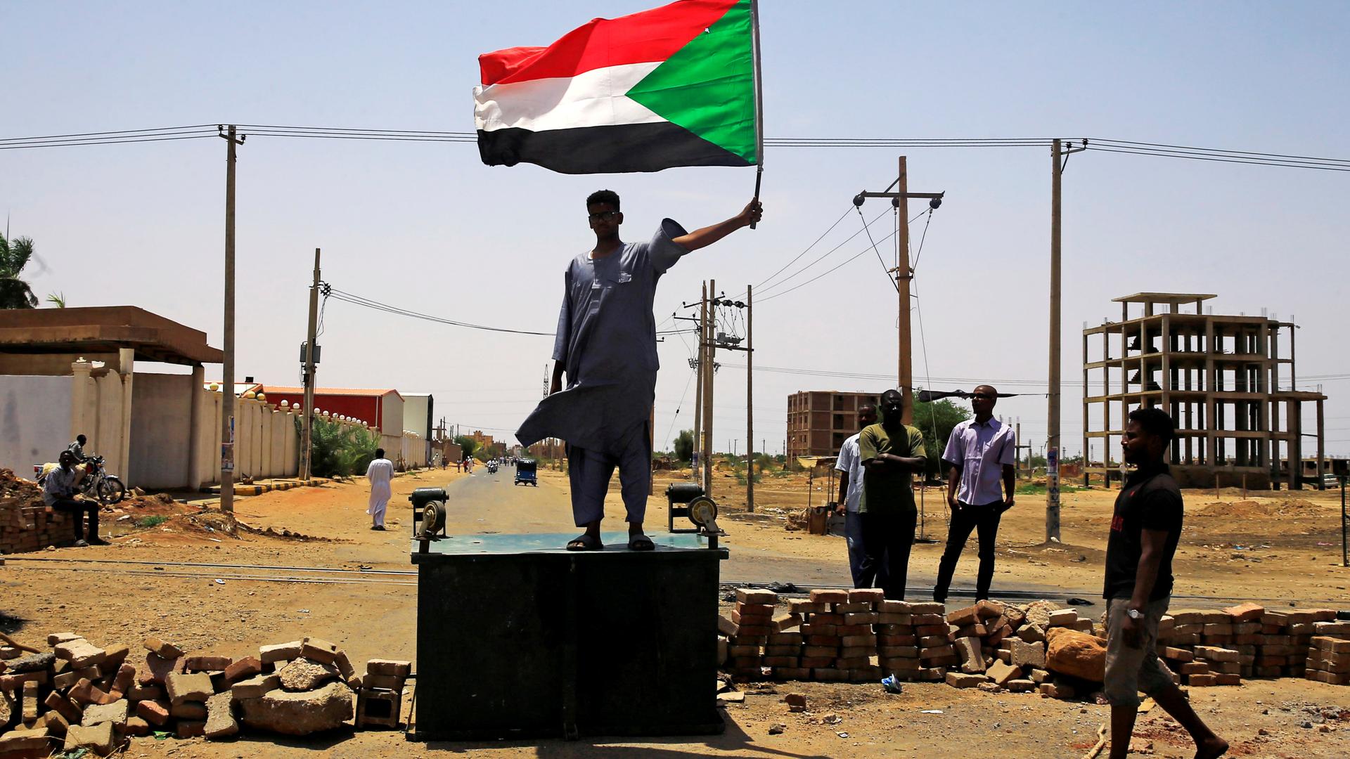 A man stands on platform holding a Sudanese flag.