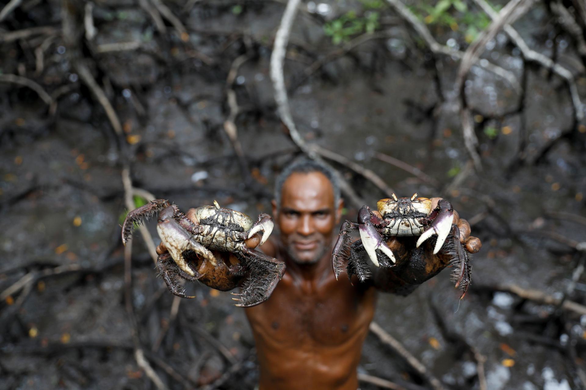 A man is shown without a shirt on holding a crab in each hand above his head.