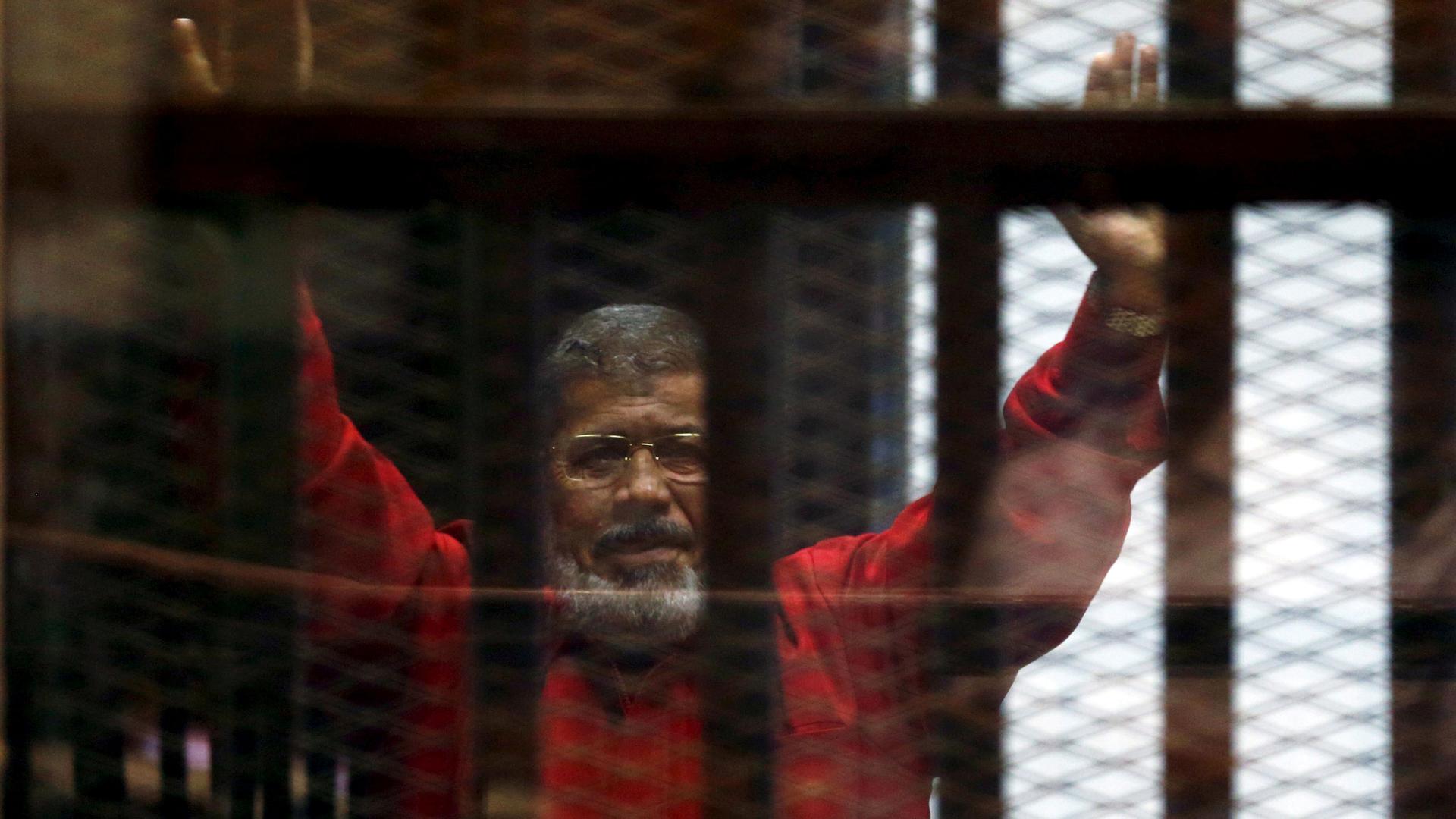 Mohammed Morsi is shown behind bars with his hands raised in the air.