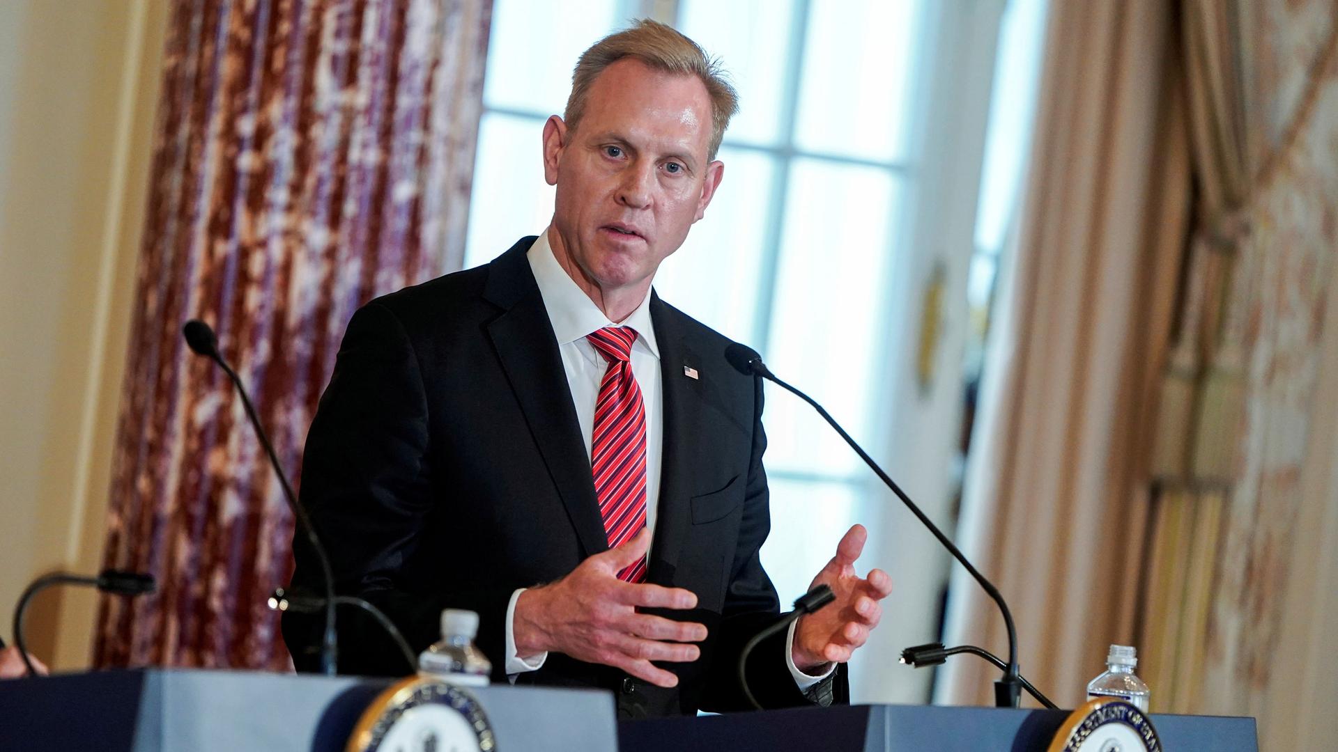 Acting US Secretary of Defense Patrick Shanahan is shown standing behind a podium with a microphone, looking to his right.