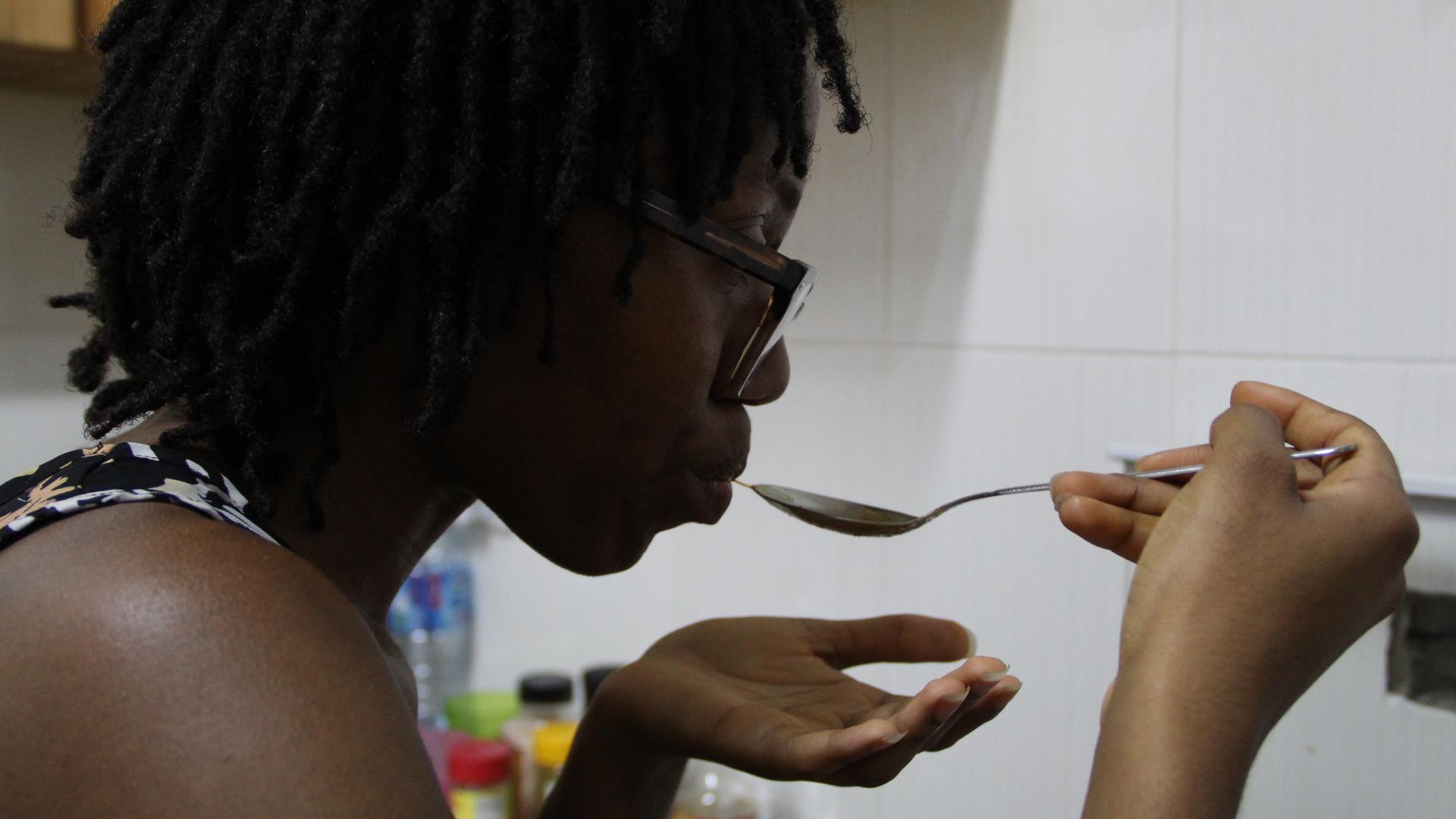 A woman samples food from a spoon. 