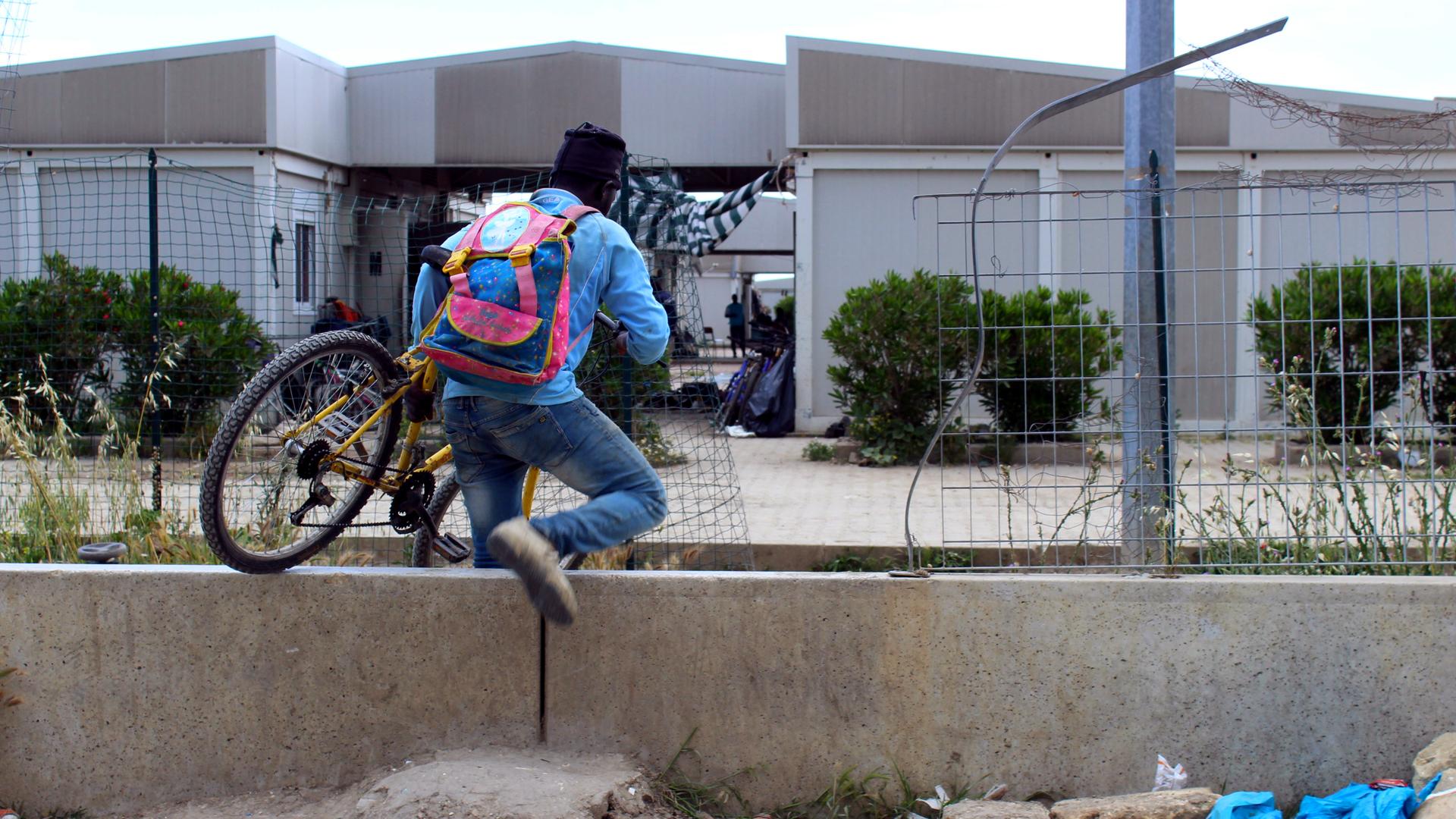 Young man crawls through fence with bicycle 