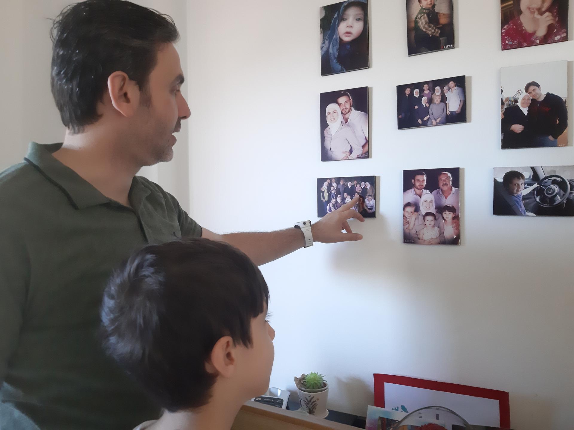 A man looks at photographs on the wall with his son