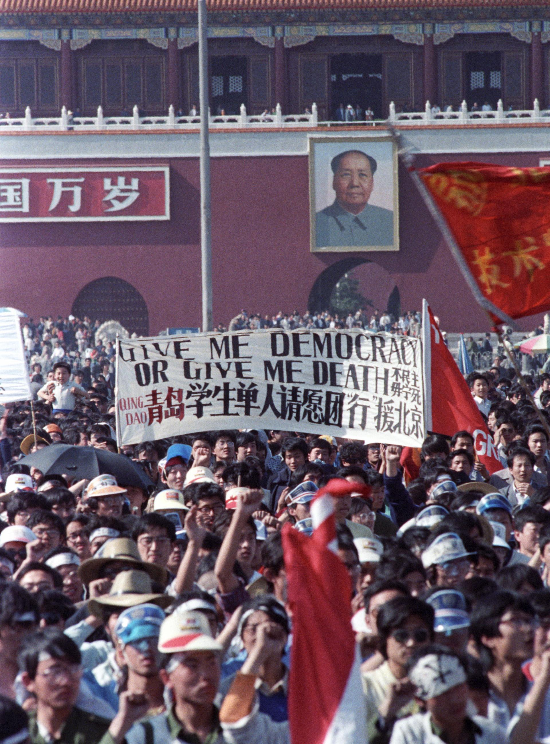 Protesters crowd Tiananmen Square and carry a banner that says 