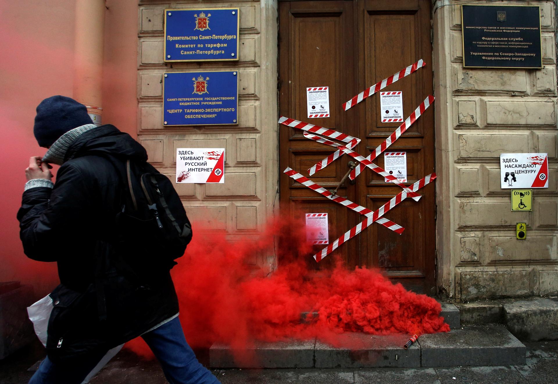 A protester walks away from a door with smoke in front of it. 
