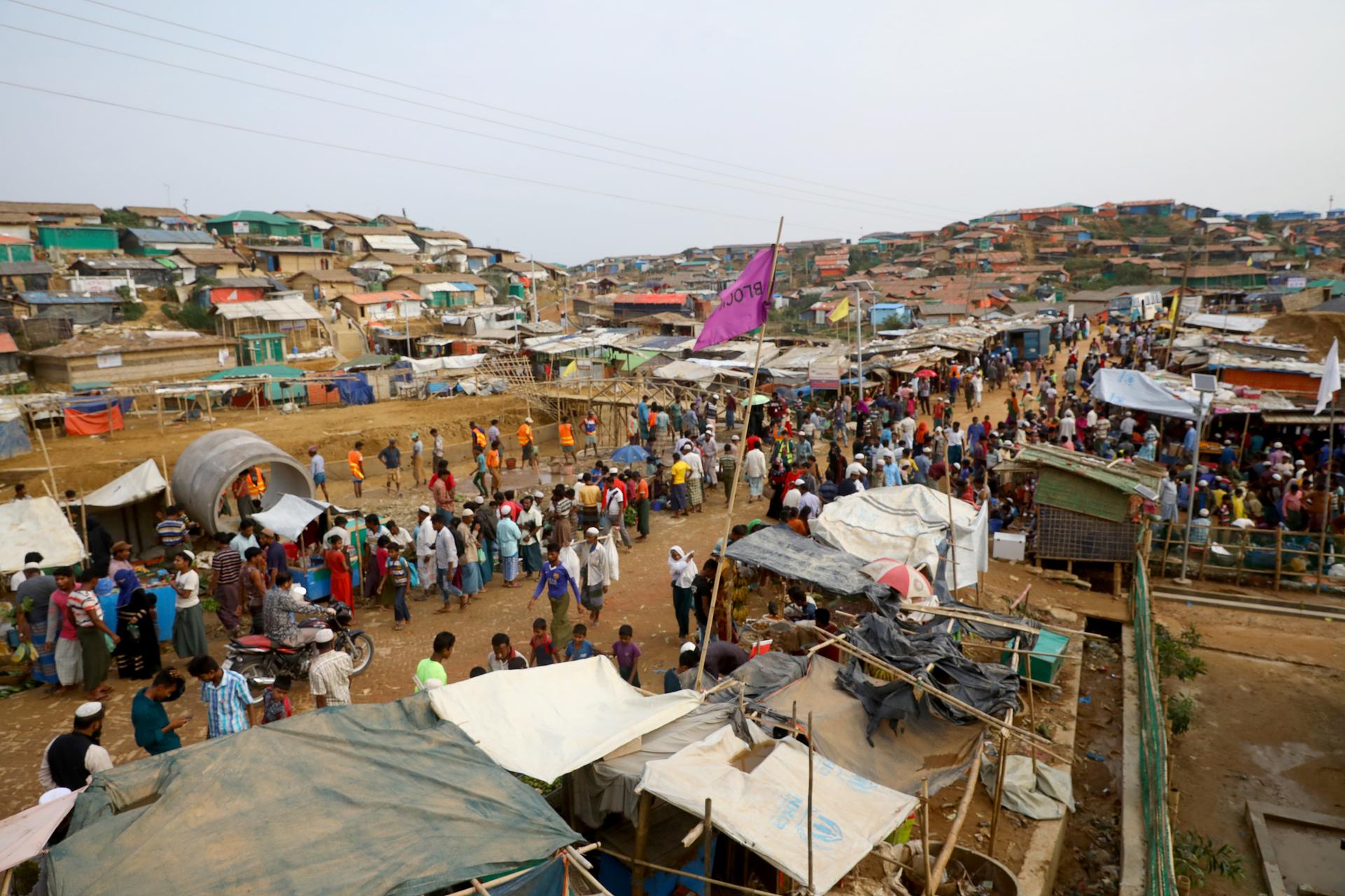 Rohingya refugees stand in a makeshift refugee camp made mostly of tents.