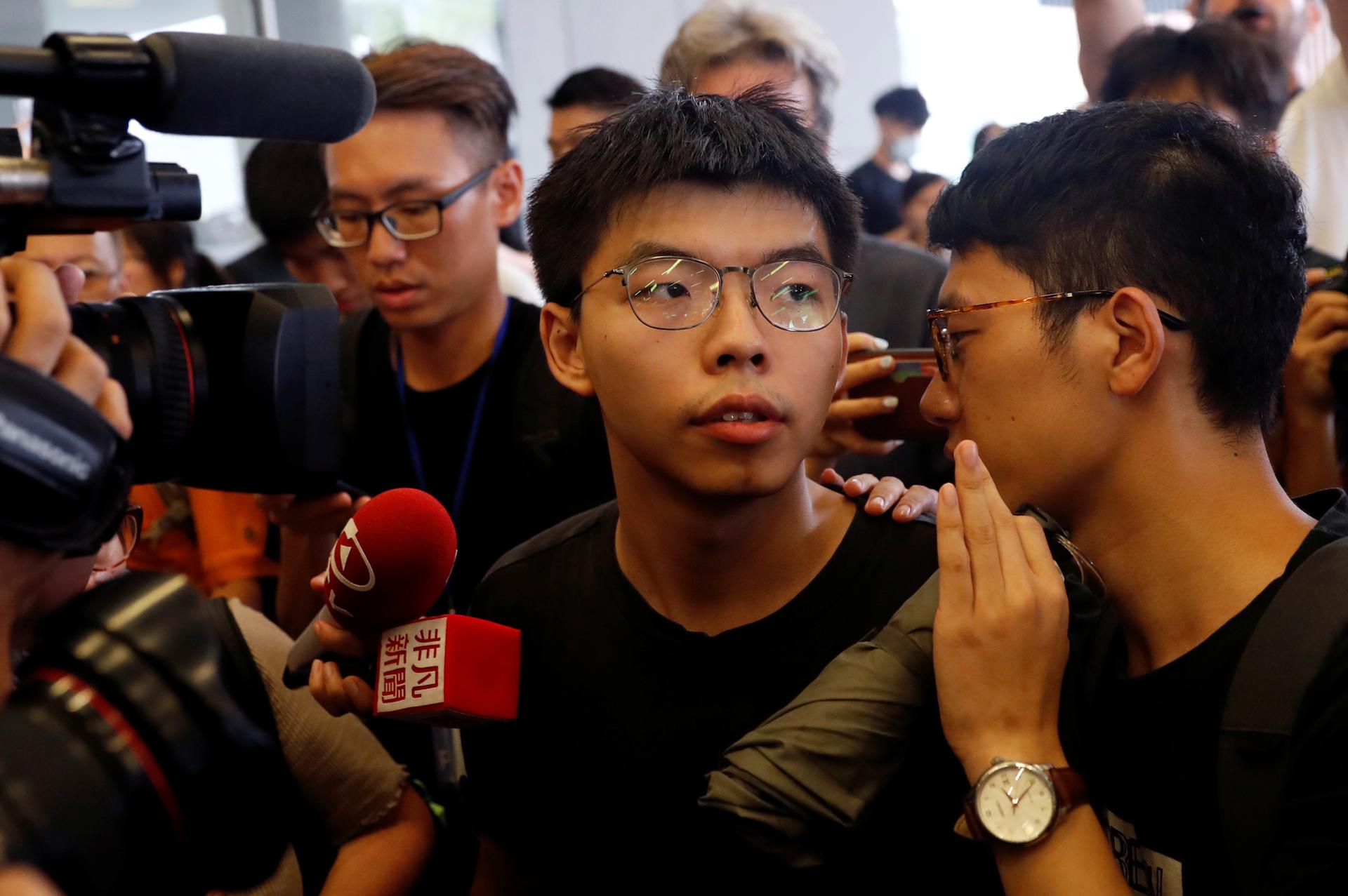 Cameras and people surround Joshua Wong as he speaks to the media. 