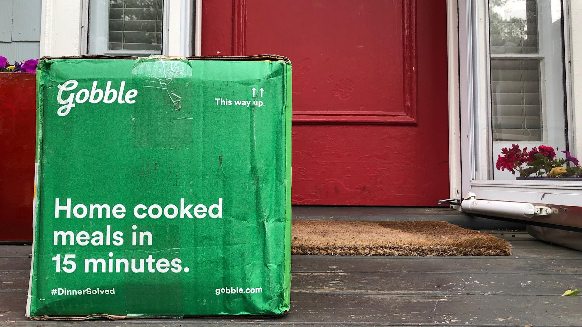 A green cardboard box sits on a door stoop.