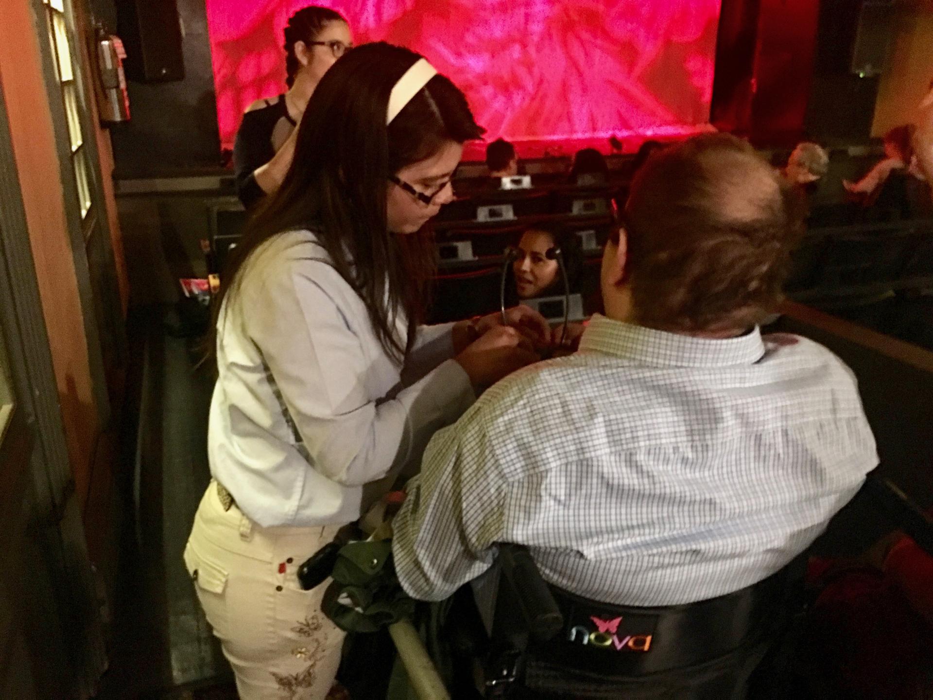 people help explain audio description equipment to visually impaired theater goers