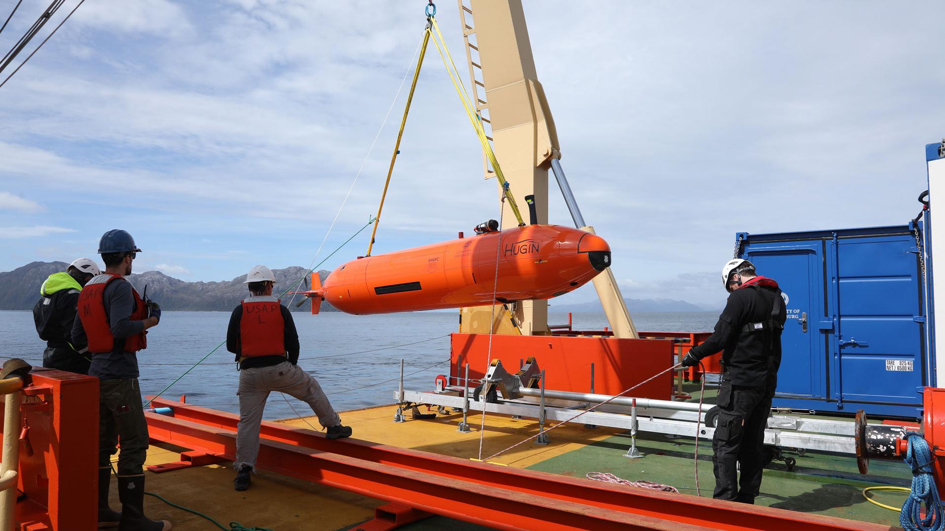 Researchers hoist the orange-colored Hugin autonomous submarine onto the deck of the Nathaniel B. Palmer.