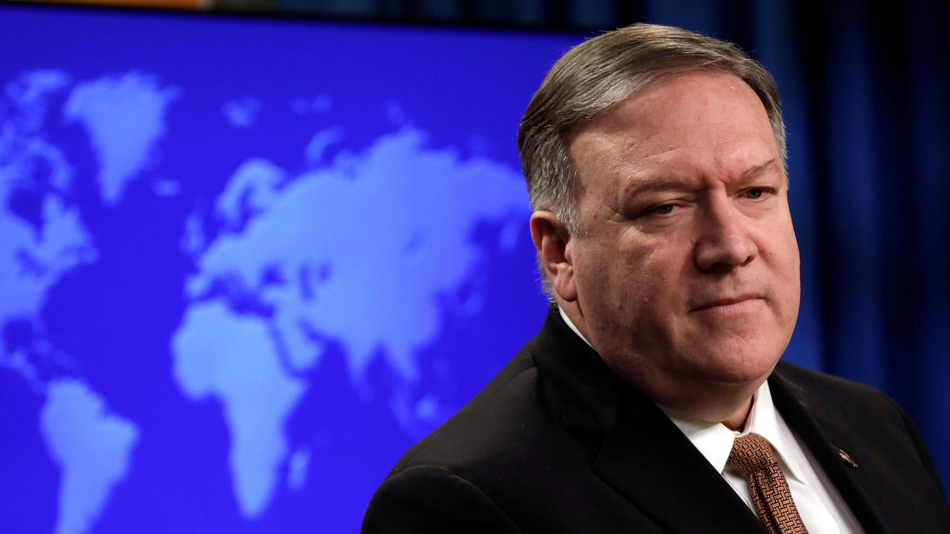 US Secretary of State Mike Pompeo is shown looking to his right and wearing a dark suit with a blue map of the globe behind him.