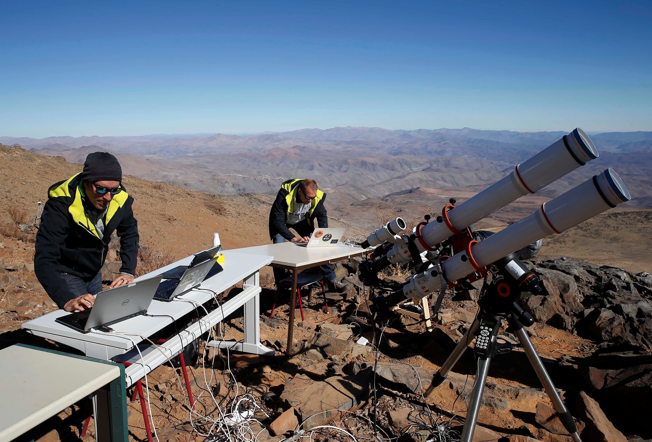 People are shown looking down at laptops with large telescopes next to them.