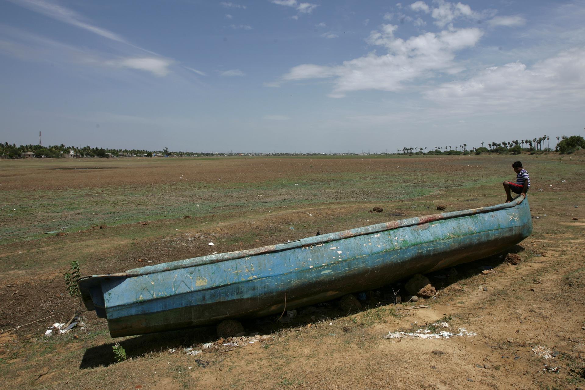 A man sits on a fishing boat stranded on the bed of dried-up lake in Thiruninravur, India, June 29, 2019.