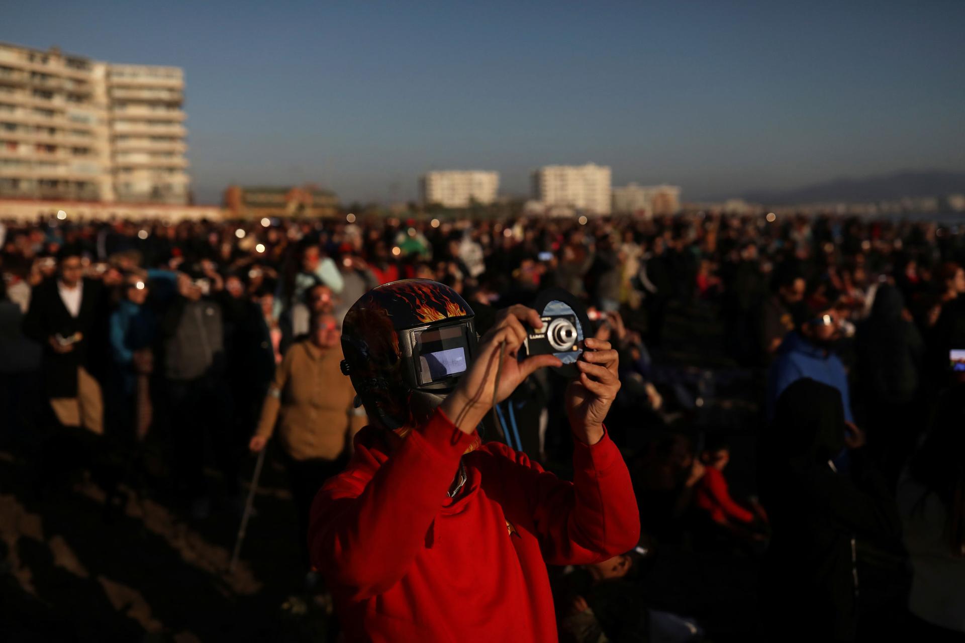 A man wearing a red sweatshirt is shown with a mask with a filter to view a the solar eclipse.