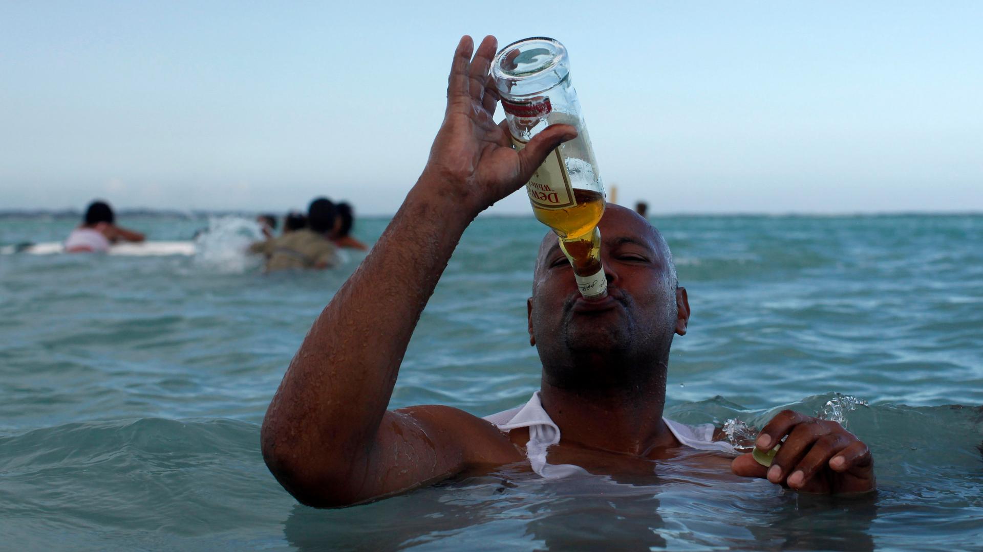 a man in the ocean drinks straight whisky from the bottle