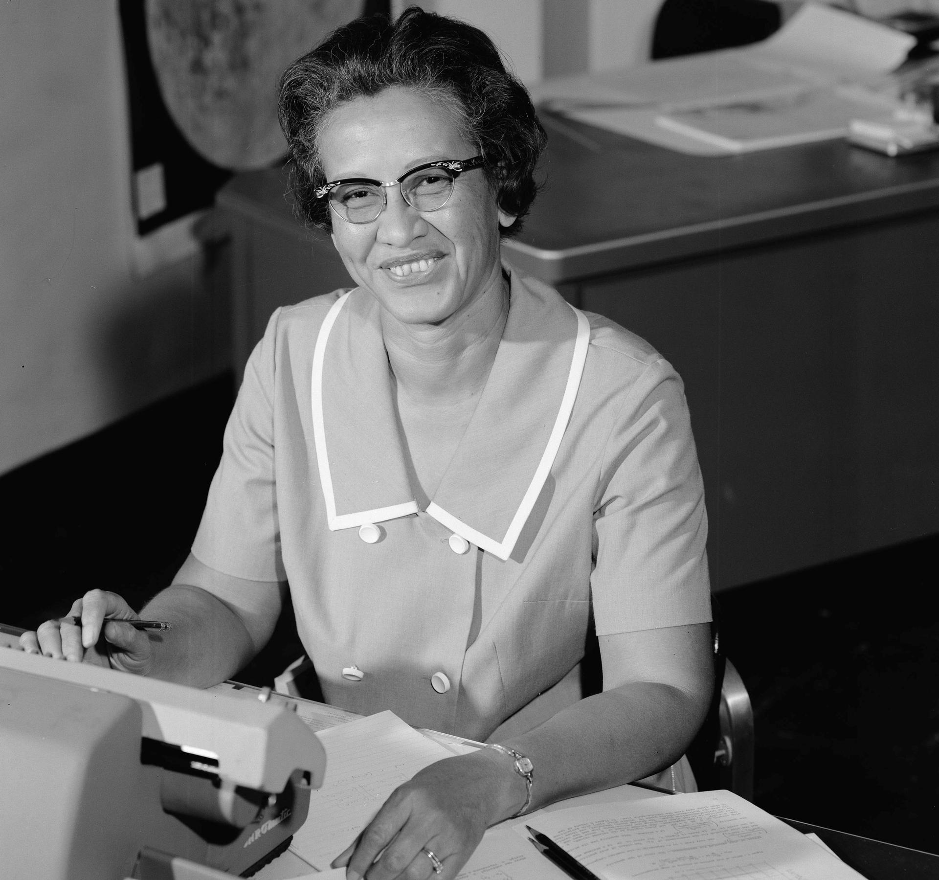 NASA research mathematician Katherine Johnson is shown in a portrait photo sitting at a desk with a typewriter on it.