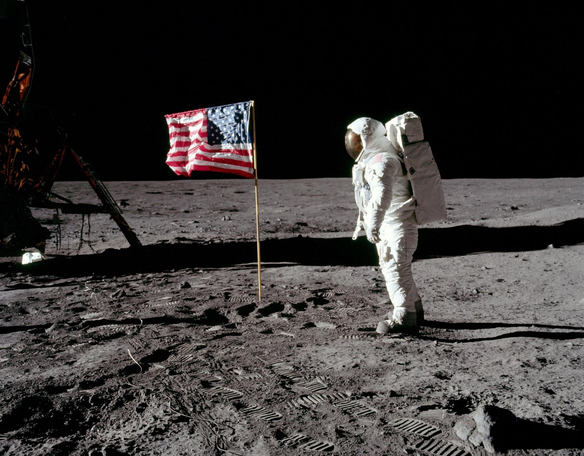 Buzz Aldrin stands in his full astronaut suit facing the United States flag.