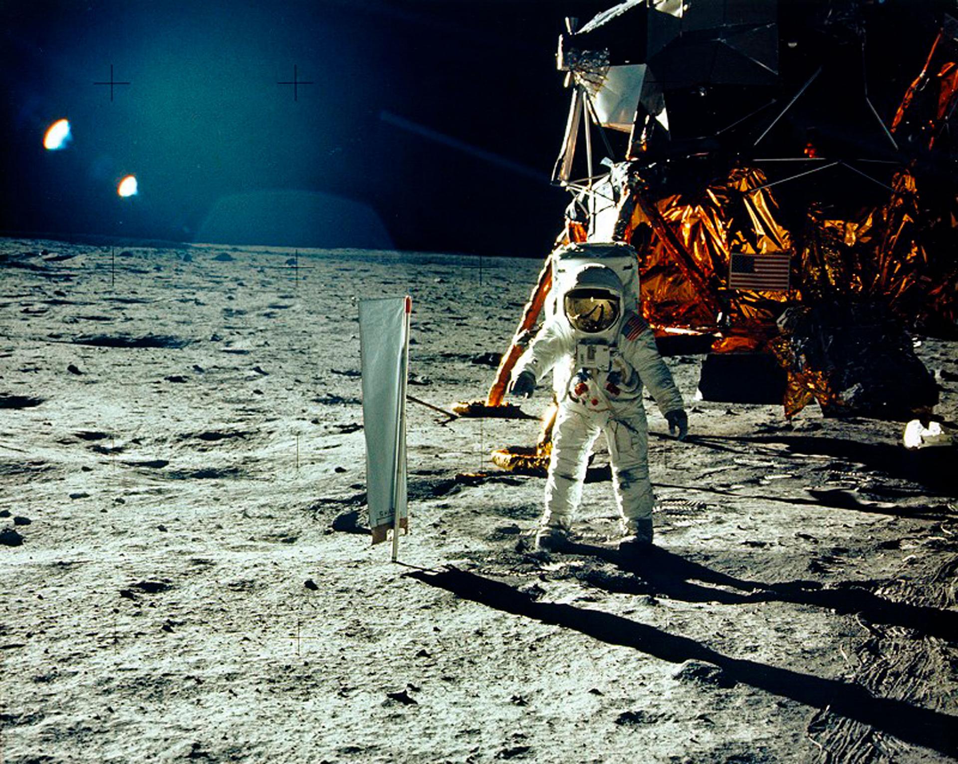 An astraunant is show in full protective gear standing on the surface of the moon.