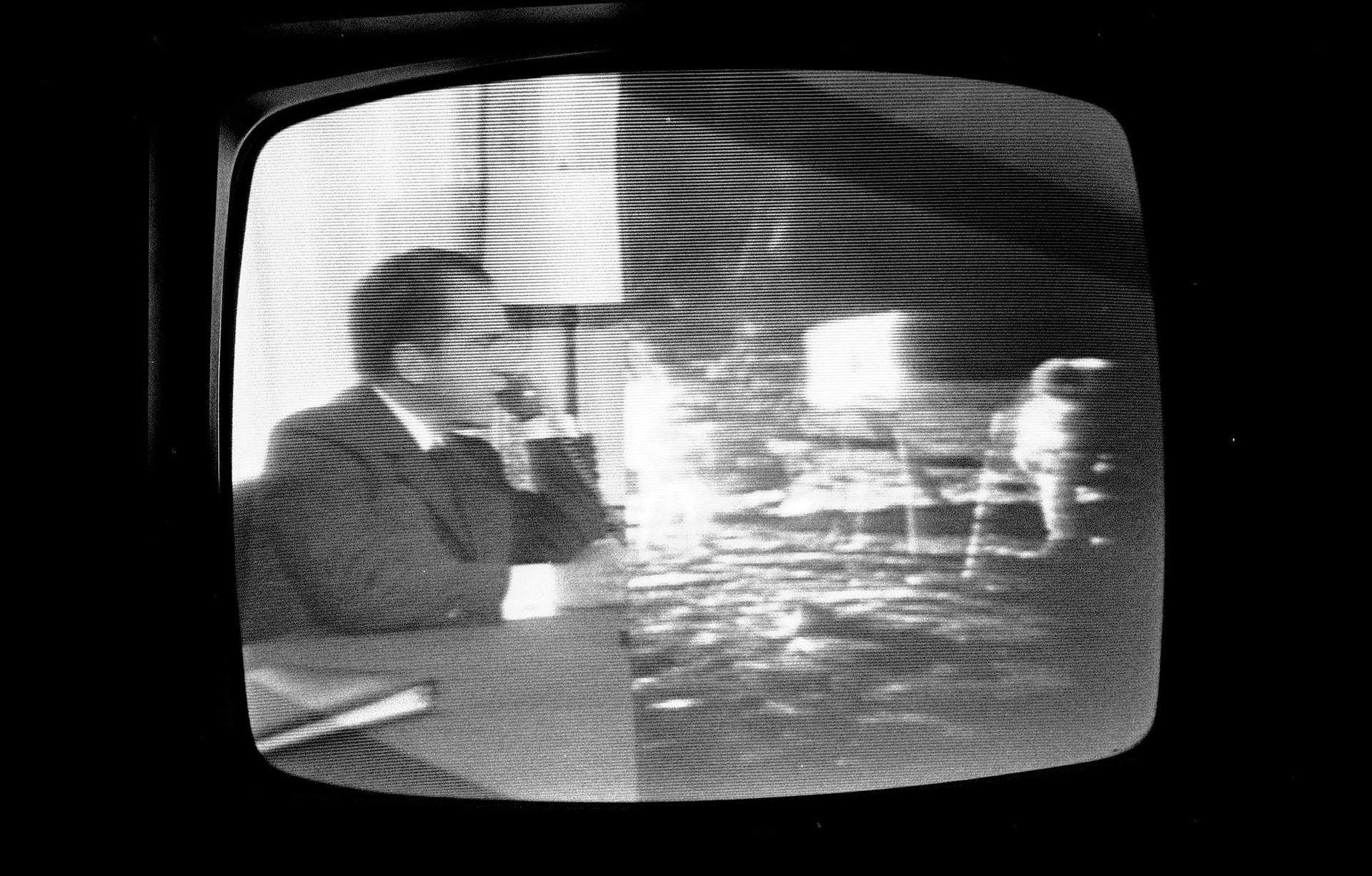 In a photograph of a television,  President Richard Nixon is shown on the left and Apollo 11 crew is shown on the right all in black and white.