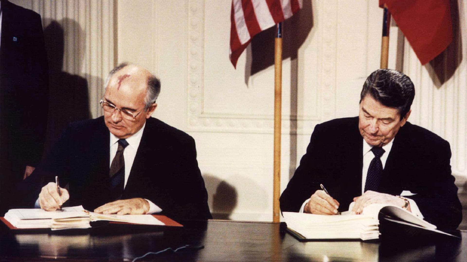 Two men sit at a desk and sign a paper