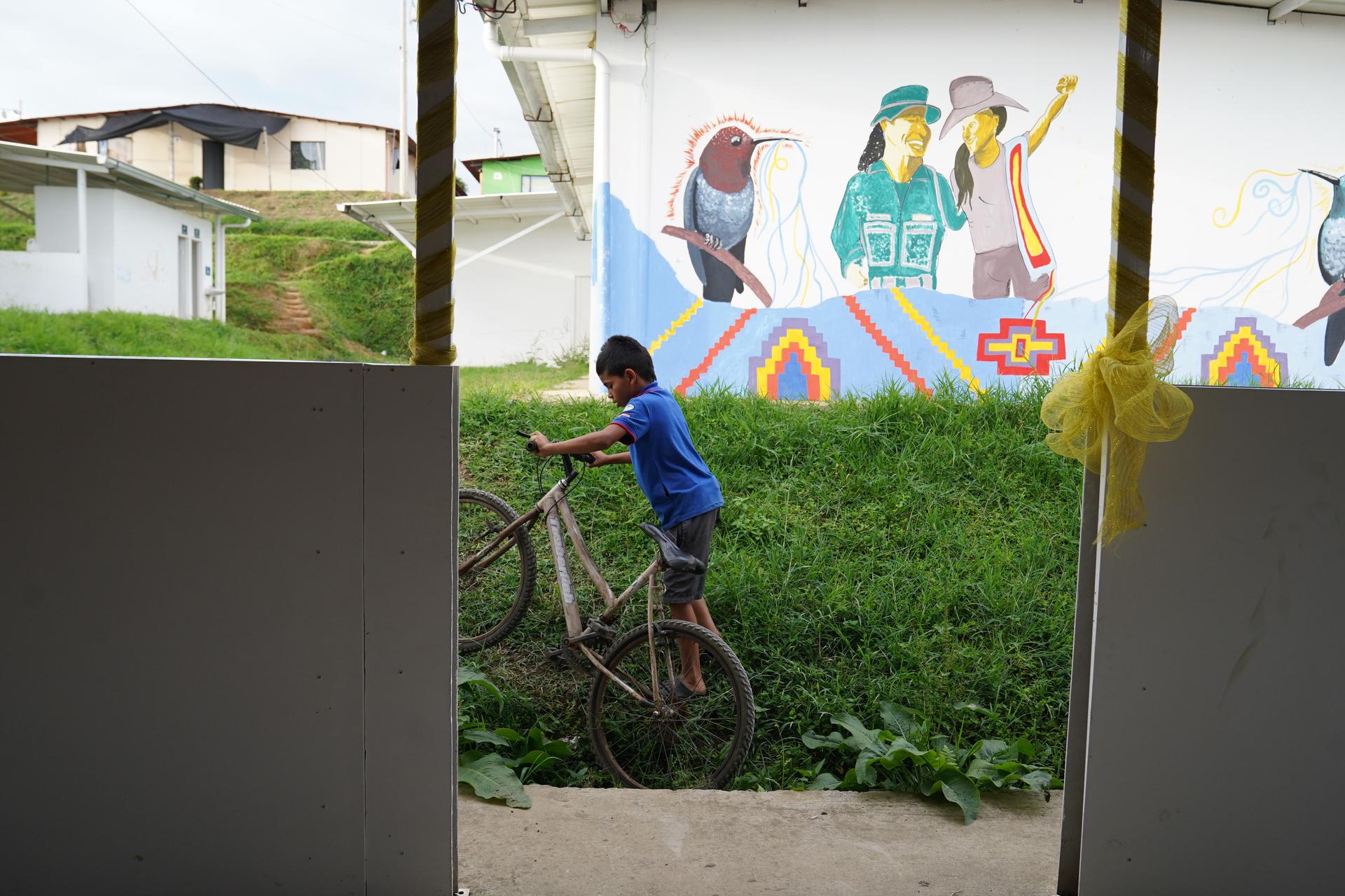 A boy rides his bike seen through a window near wall with mural