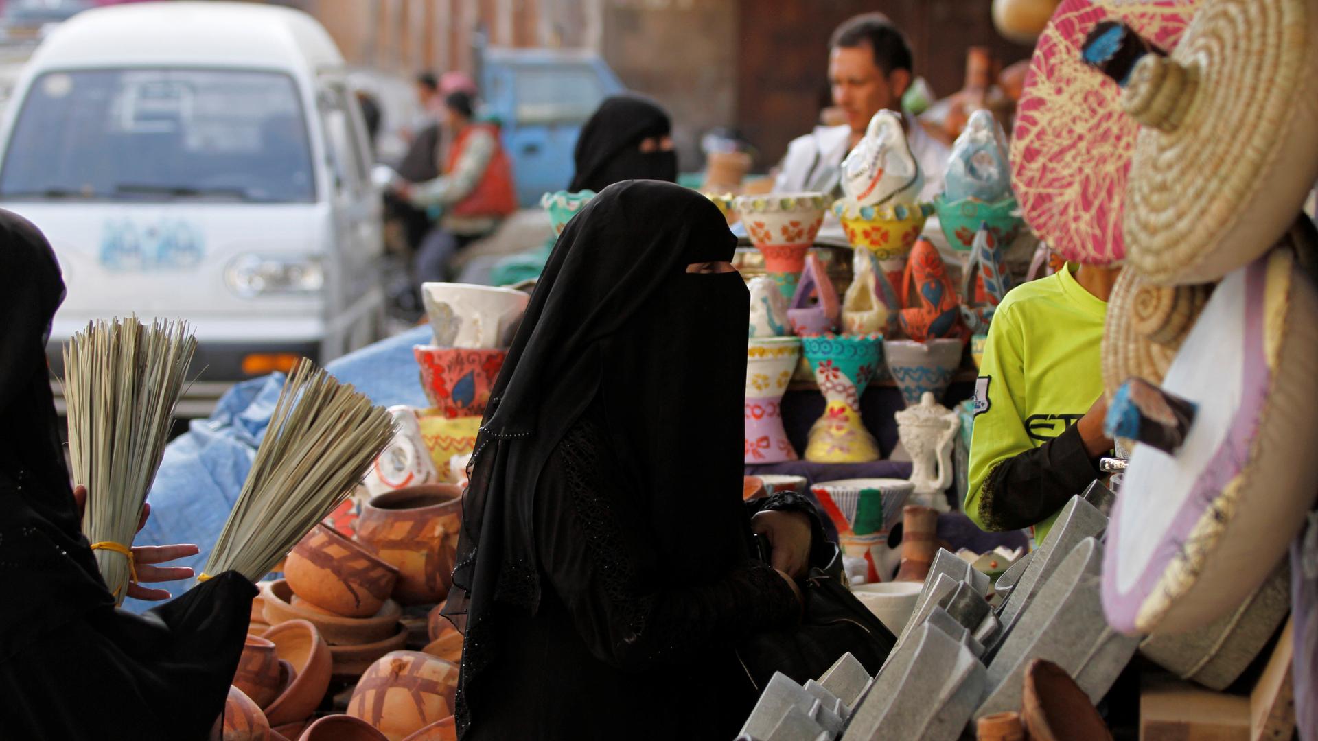 Women in black hijab shop at market in Sanaa, Yemen
