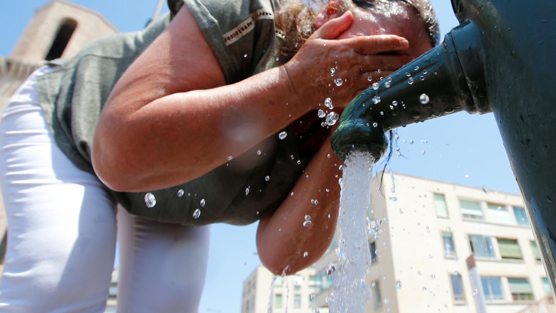 A woman cools off by splashing water on her face. 