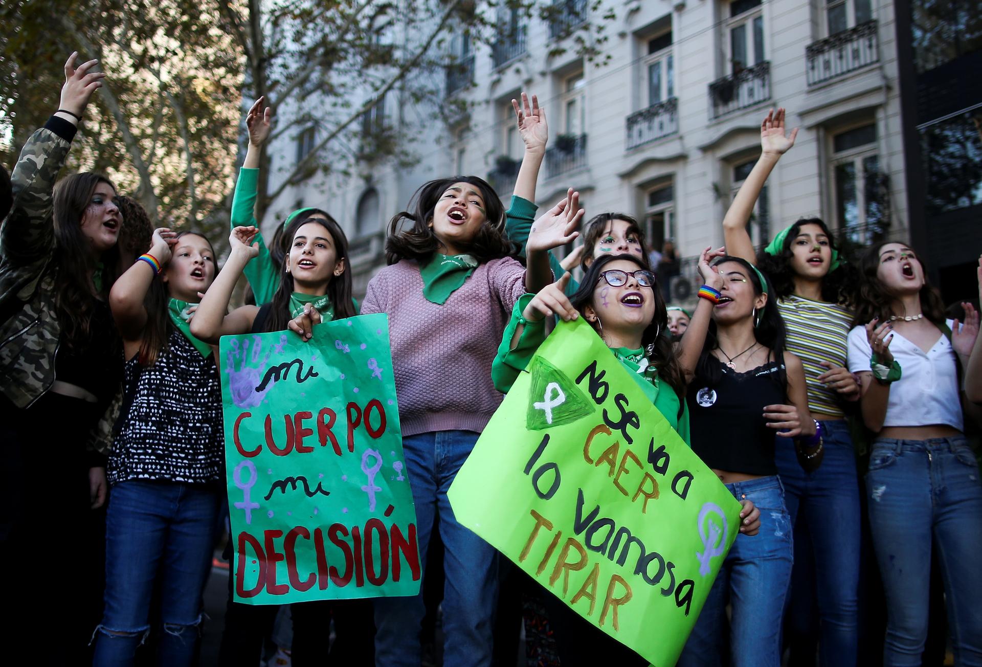 Women stand together and hold sings in Spanish in a city. 