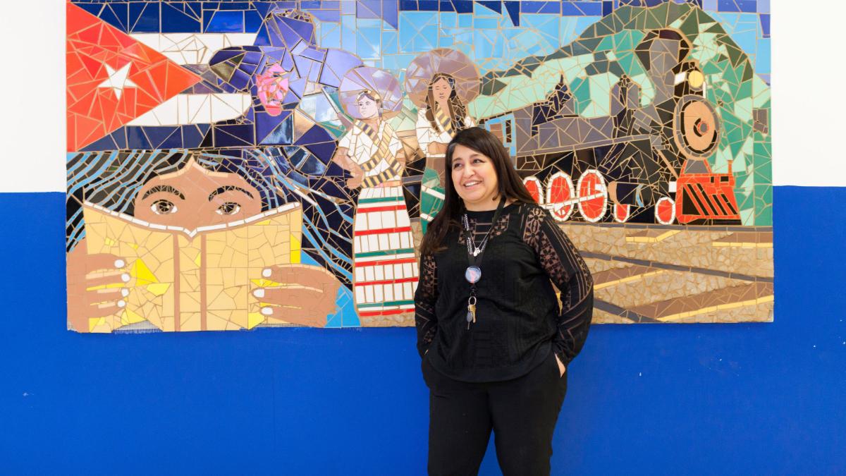 Woman in a black suit poses in front of a tile mural.