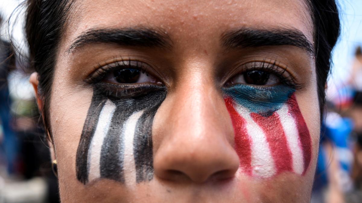 A woman with a Puerto Rican flag painted on her face looks at the camera.