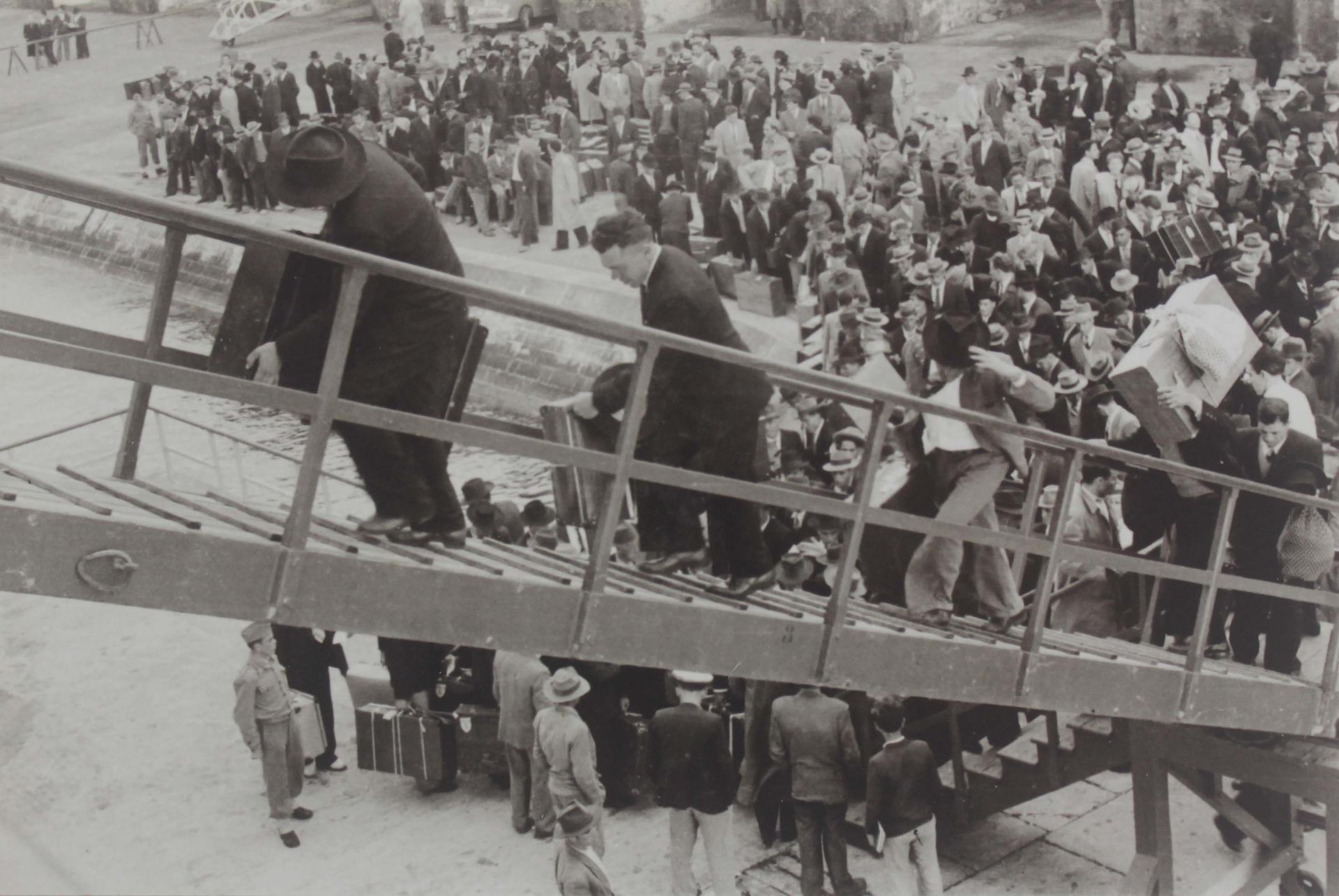 A black and white photo of men ascending to a ship, with others on the quay below