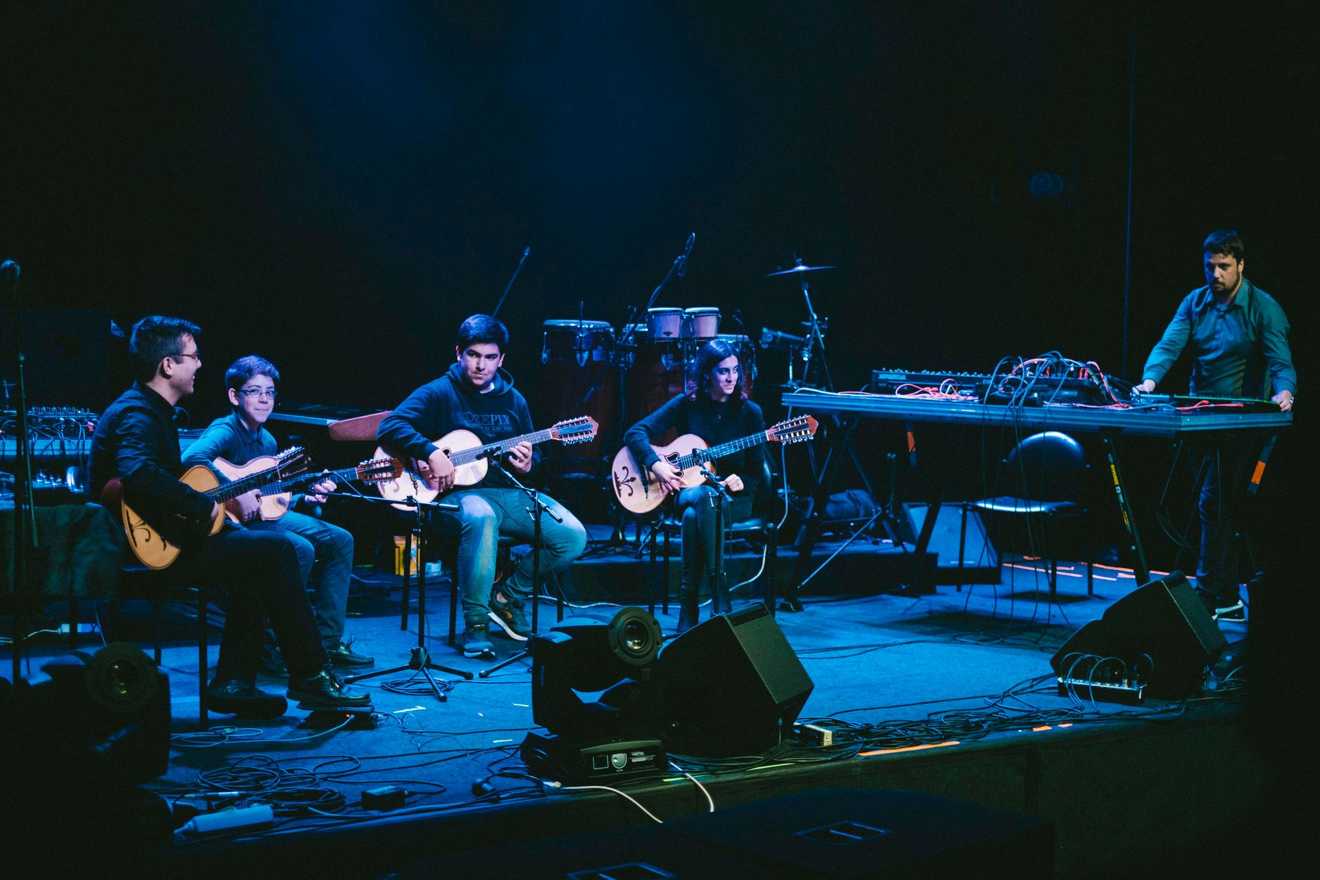 Musicians sit on a stage in blue lighting