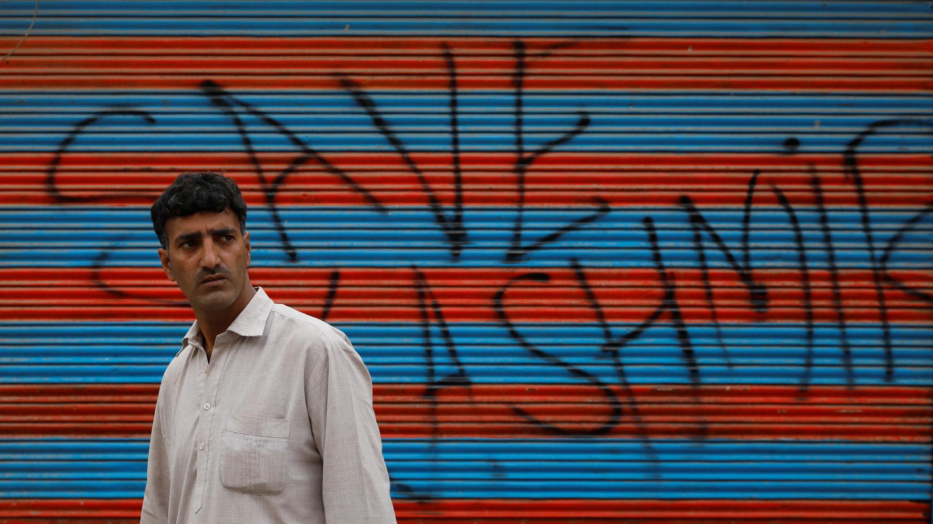 A man walks in front of a wall spray painted with the words "Save Kashmir"