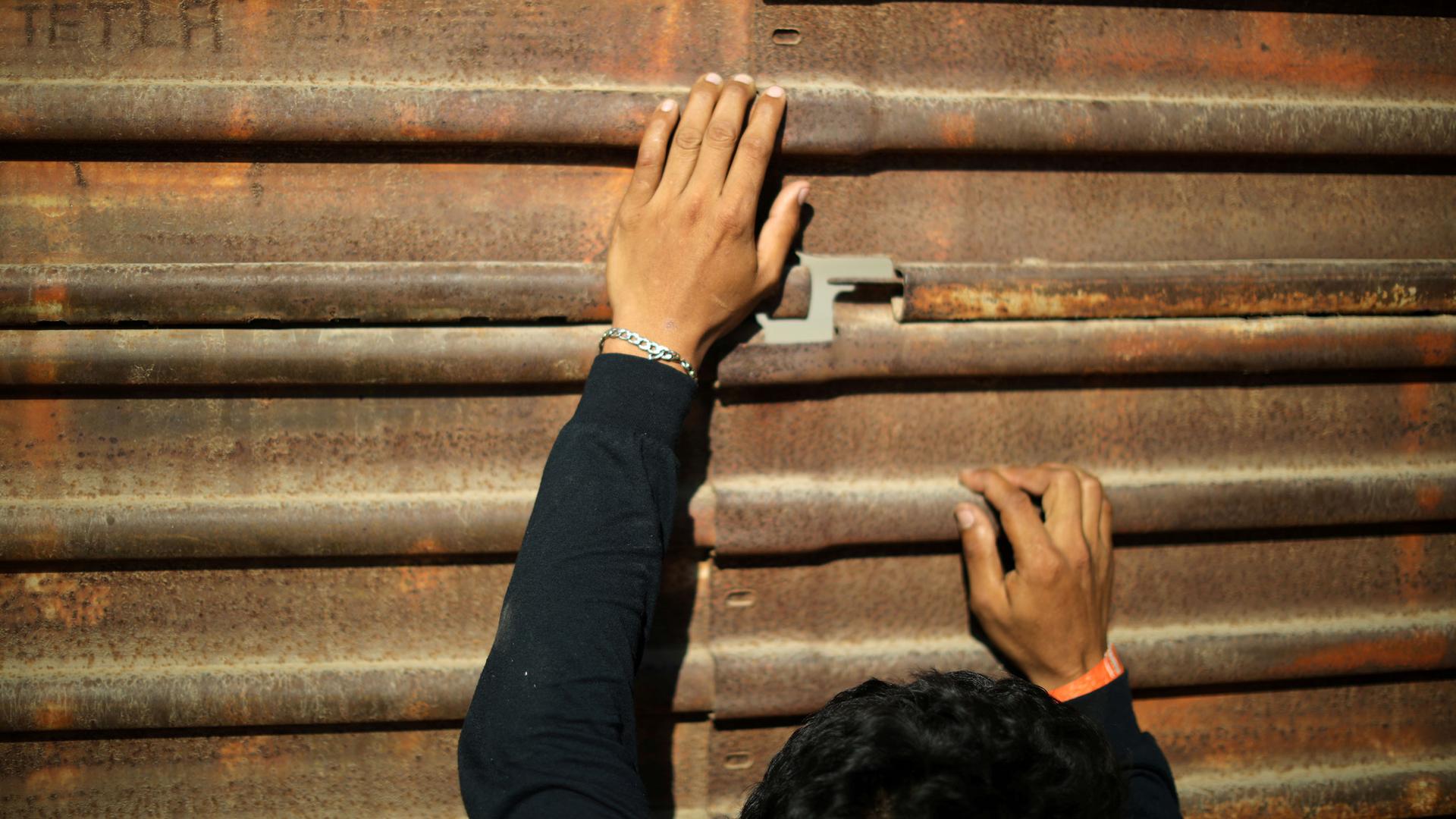 A persons hands hand onto the metal of the border wall