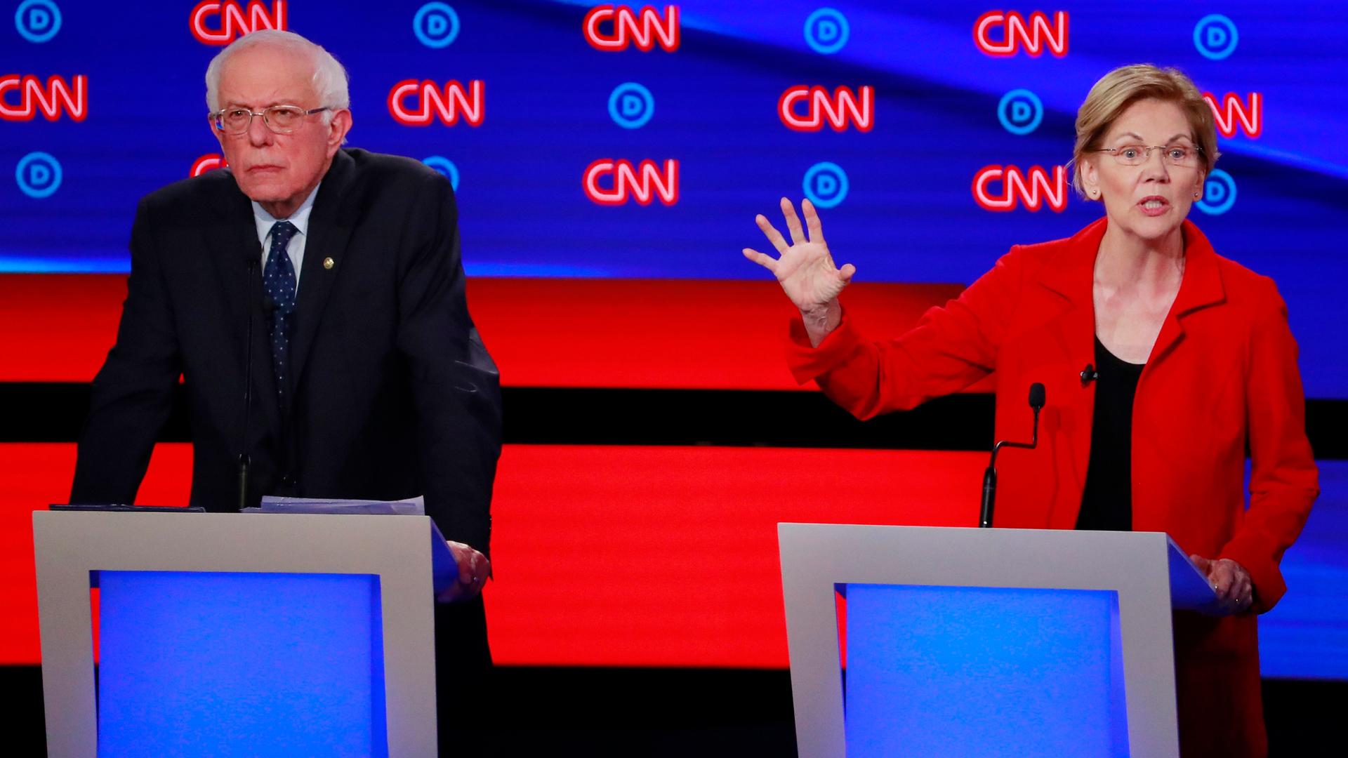 Bernie Sanders and Elizabeth Warren each stand at their podiums on the debate stage