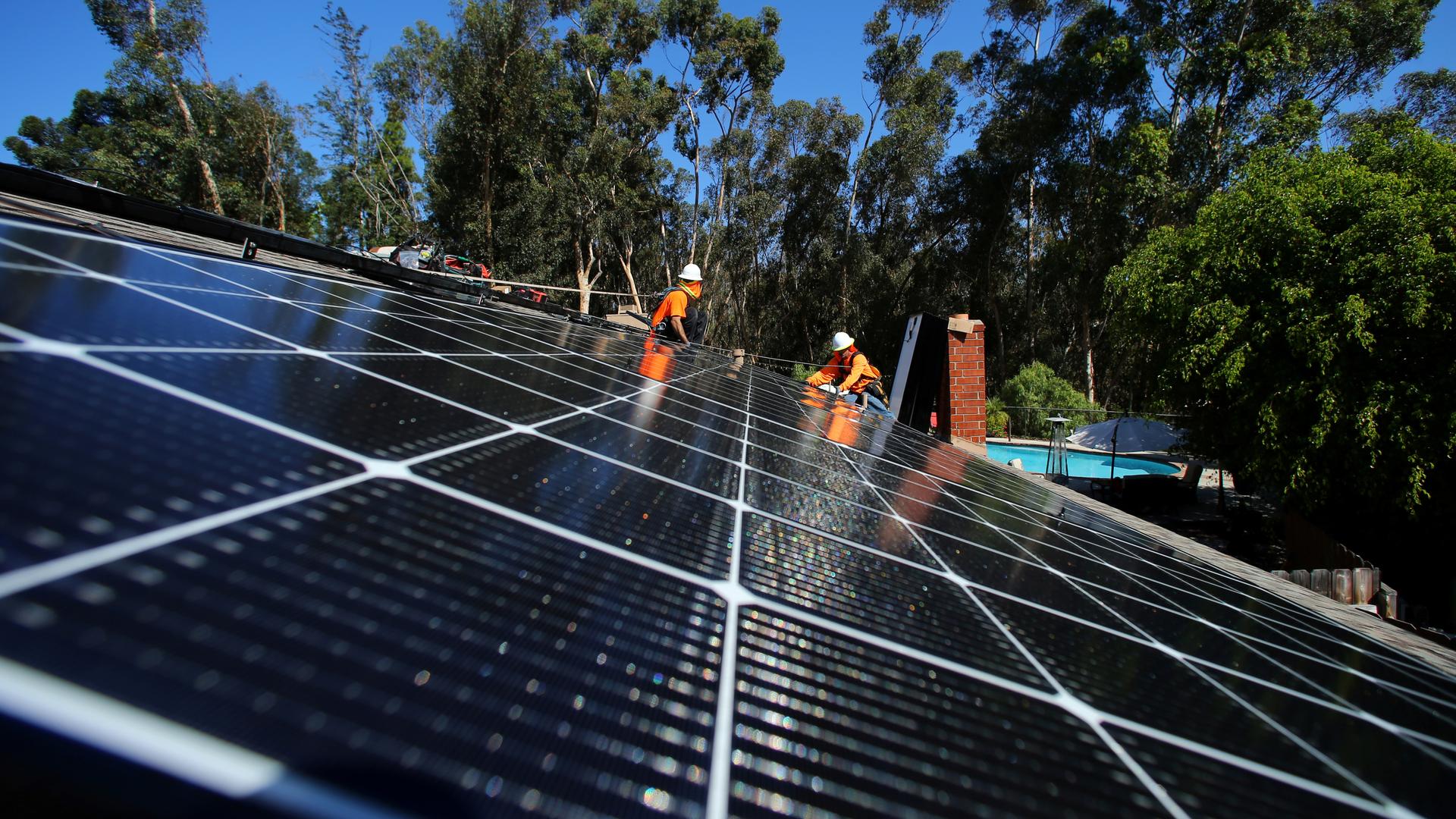 workers intsall solar panels on a rooftop in california