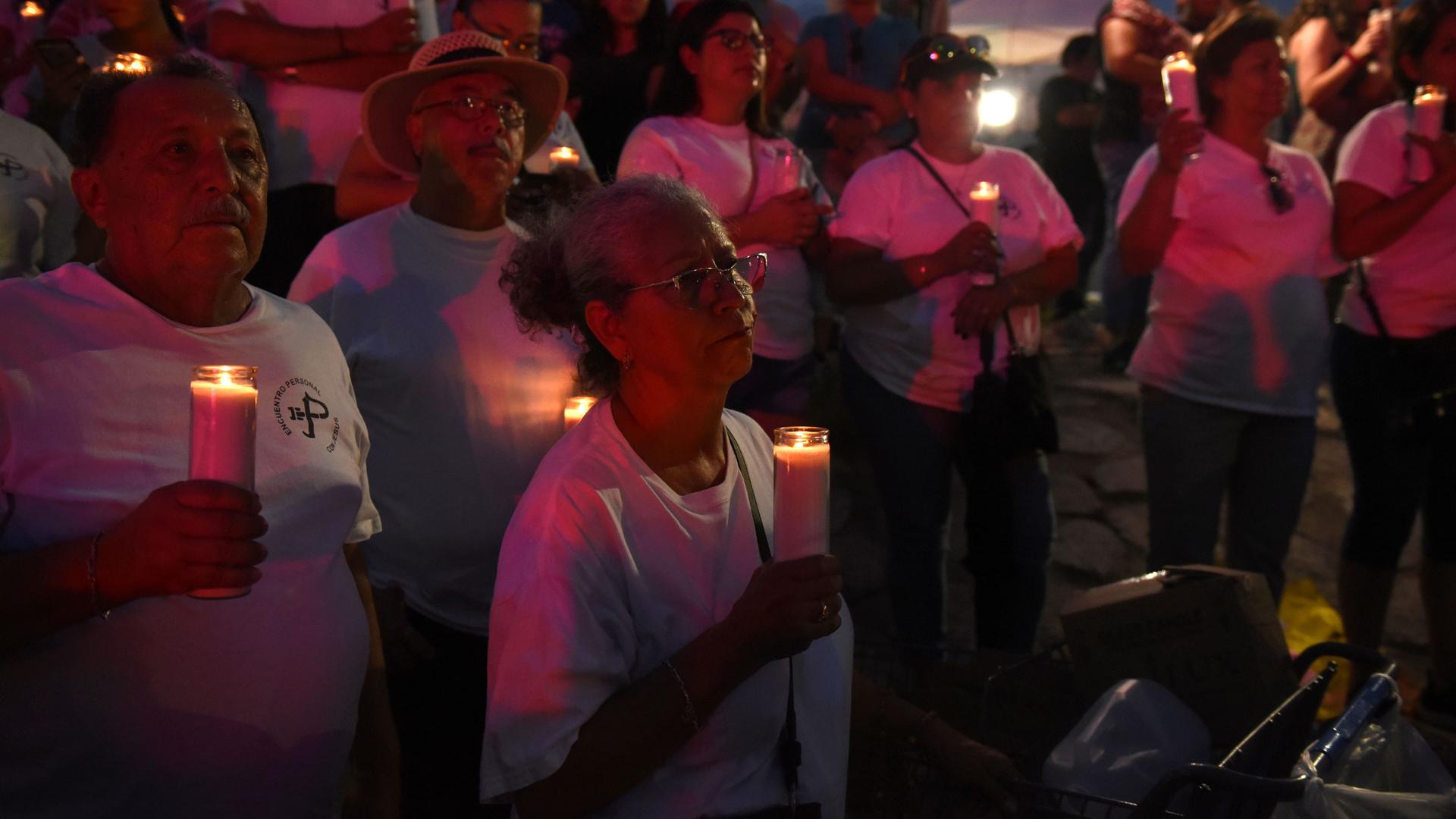 A group of people hold candles during a vigil at a memorial.
