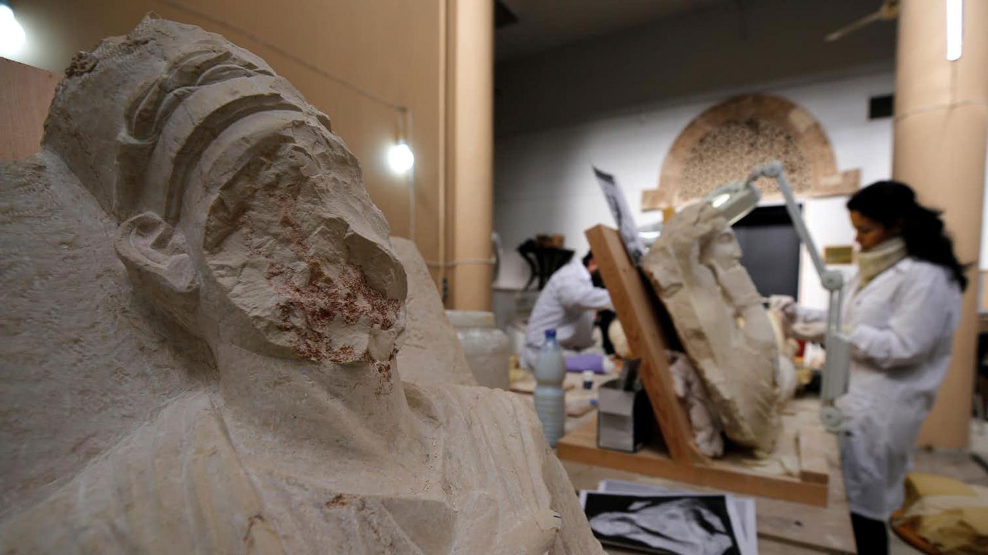 A woman works on damaged statues - one is missing part of its face - from Palmyra at Syria’s National Museum of Damascus