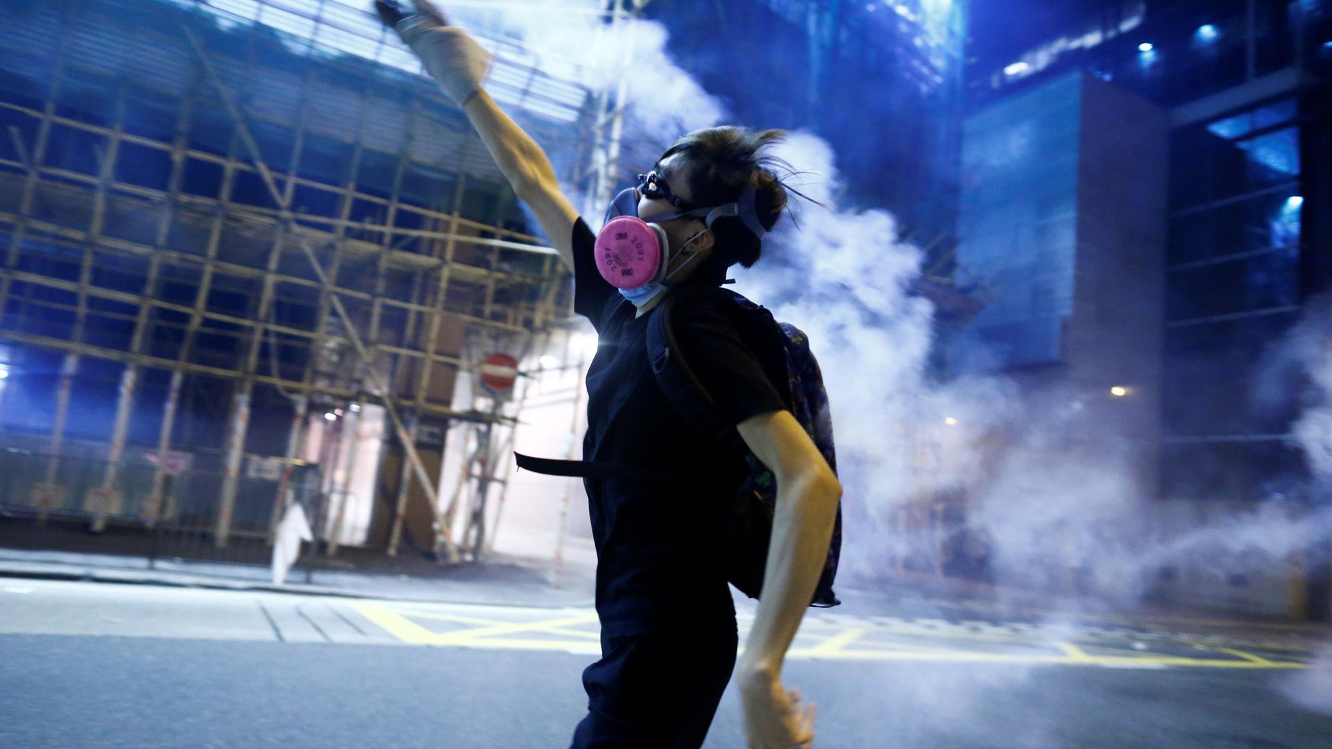 A protester throws a tear gas cartridge against a dark, blue background
