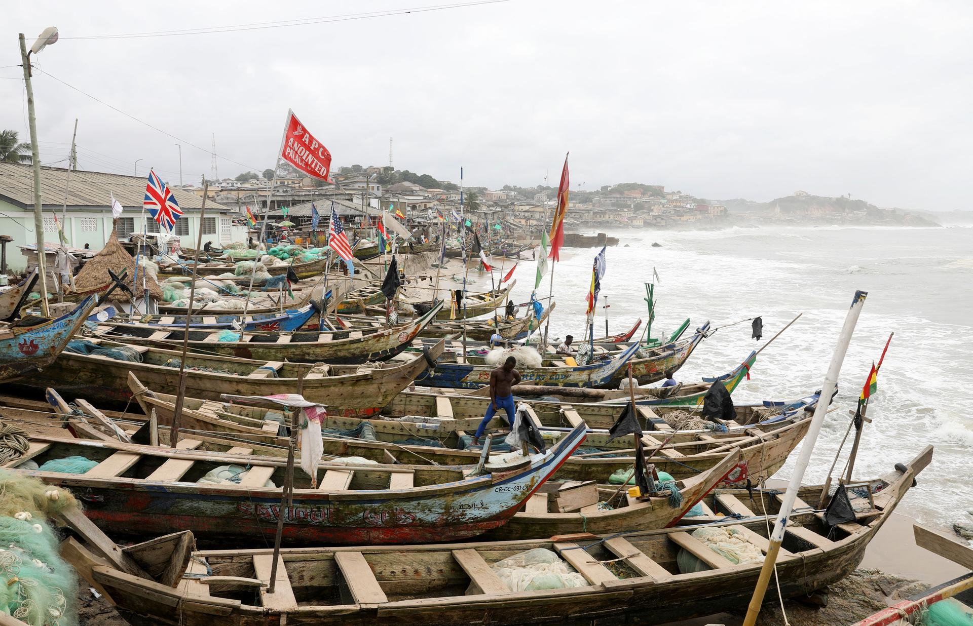 Several long wooden boats are shown in a row on the beach.